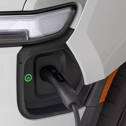 A NACS charging cable plugged into the charging port of a white Rivian electric vehicle.