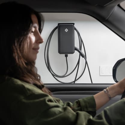A woman sitting inside her Rivian EV. Her Rivian Wall Charger can be seen through the driver window.