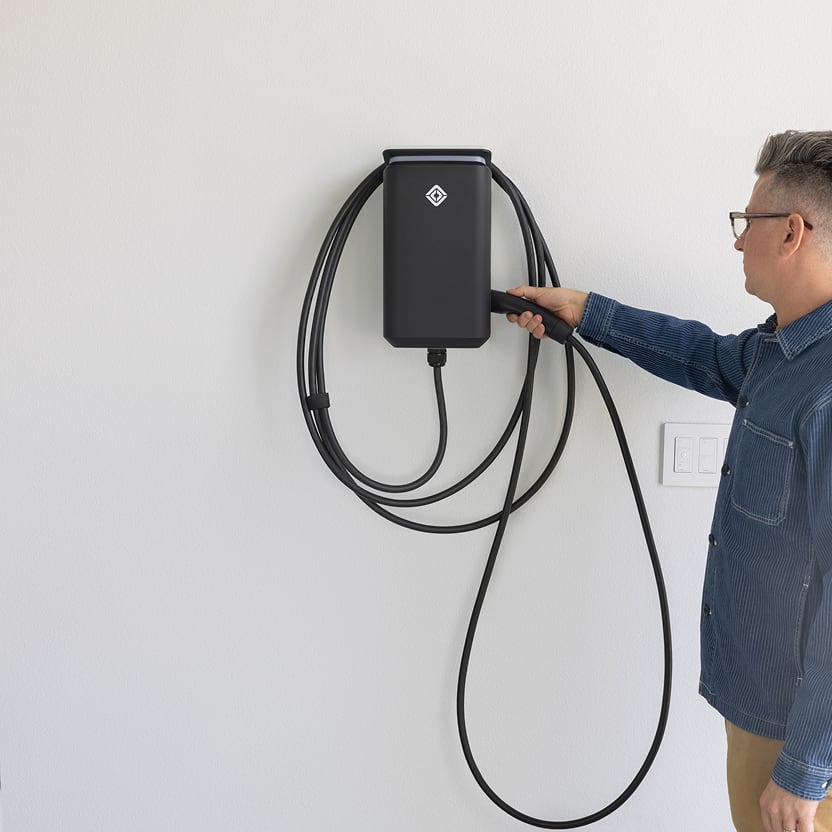 A man reaching for the cord of their Rivian Wall Charger, installed against a plain white wall in their garage.