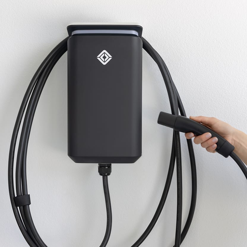 A hand hold the cord of a Rivian Wall Charger.