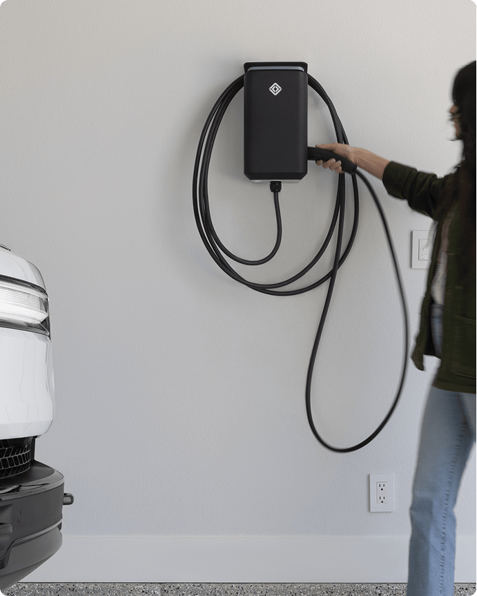 Woman in a dark jacket and light jeans is about to use her Rivian Wall Charger.