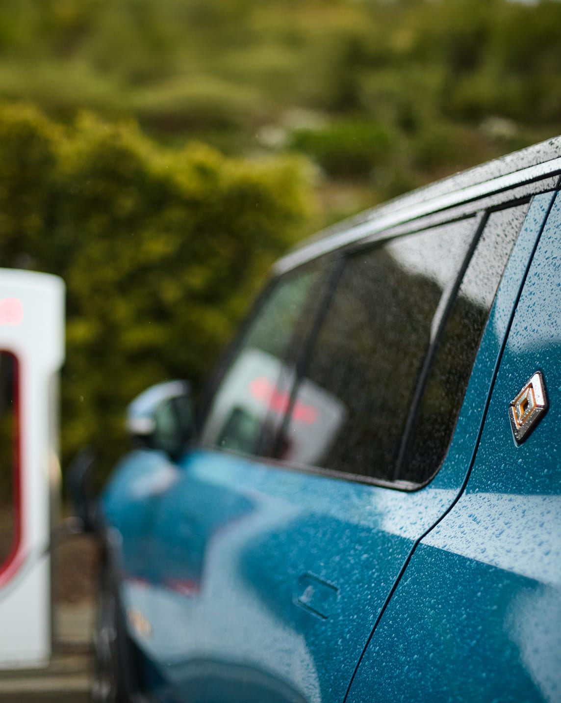 Rivian Blue vehicle with raindrops on it parked at an EV charger.