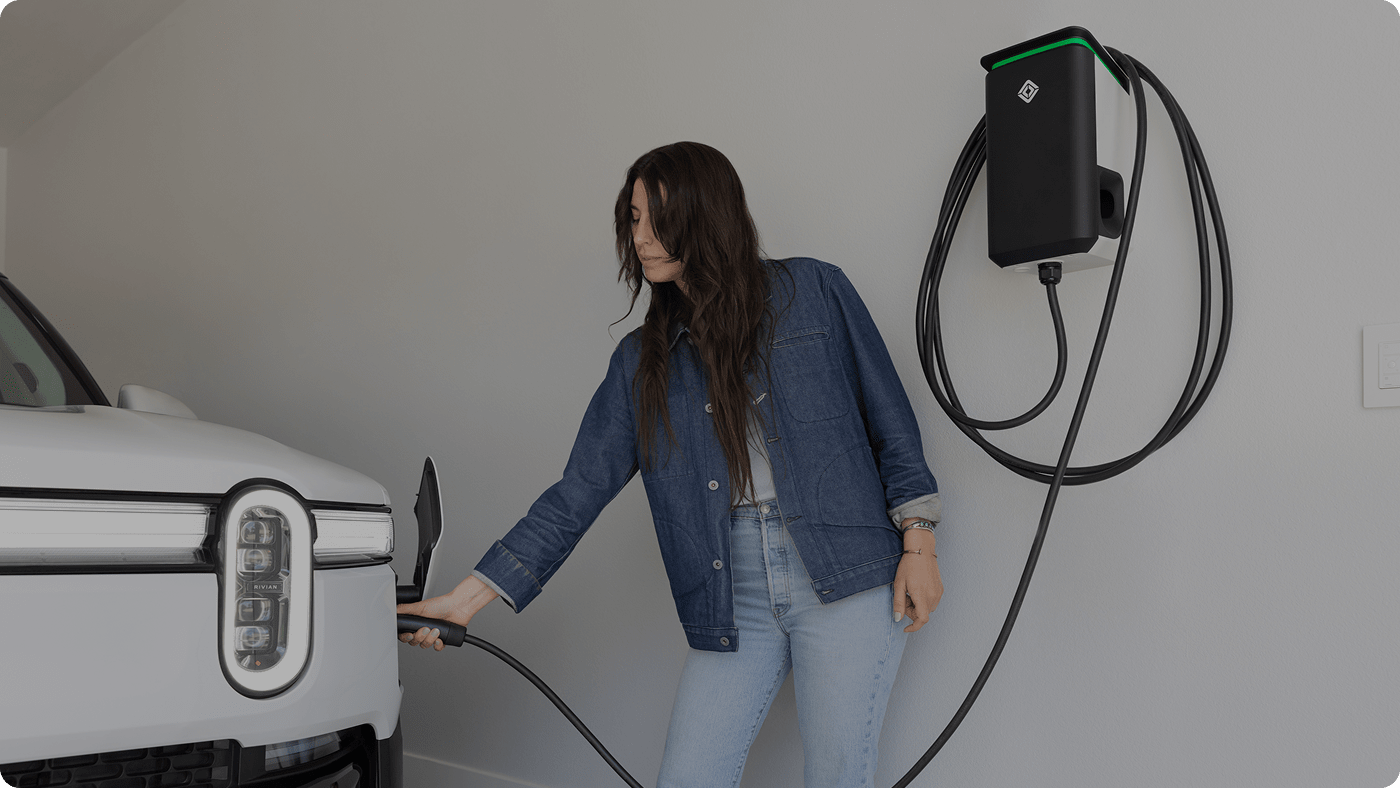 Woman in dark denim jacket and light jeans using a Rivian Wall Charger in her garage.