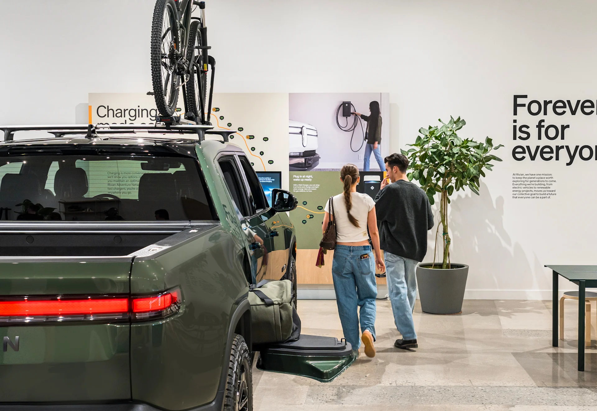 Two people walking beside a dark green Rivian R1T electric truck inside the Rivian King of Prussia.