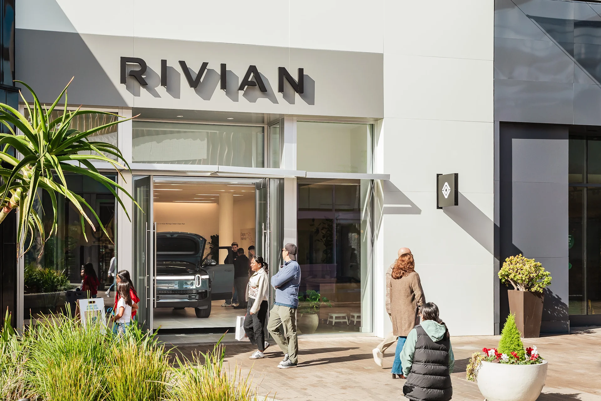 The front of the Rivian La Jolla space storefront in San Diego. A father and a child inside as they walk inside.