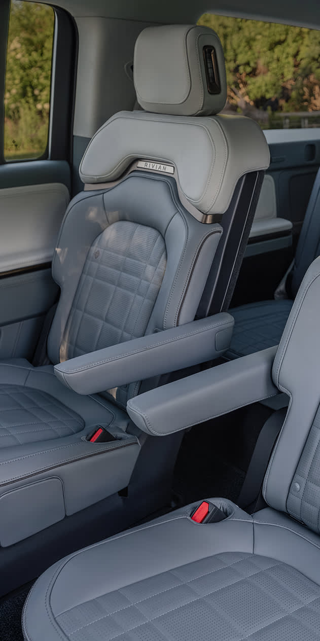 Interior view of a Rivian R1S featuring second-row captain's chairs and a third-row bench seat in two-tone light gray vegan leather.