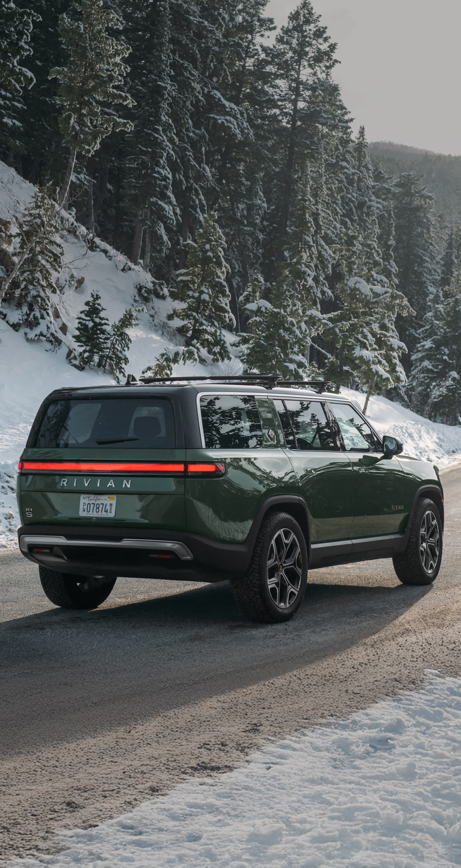 A back-side view of a Green Rivian R1S electric SUV traveling down a snowy road.