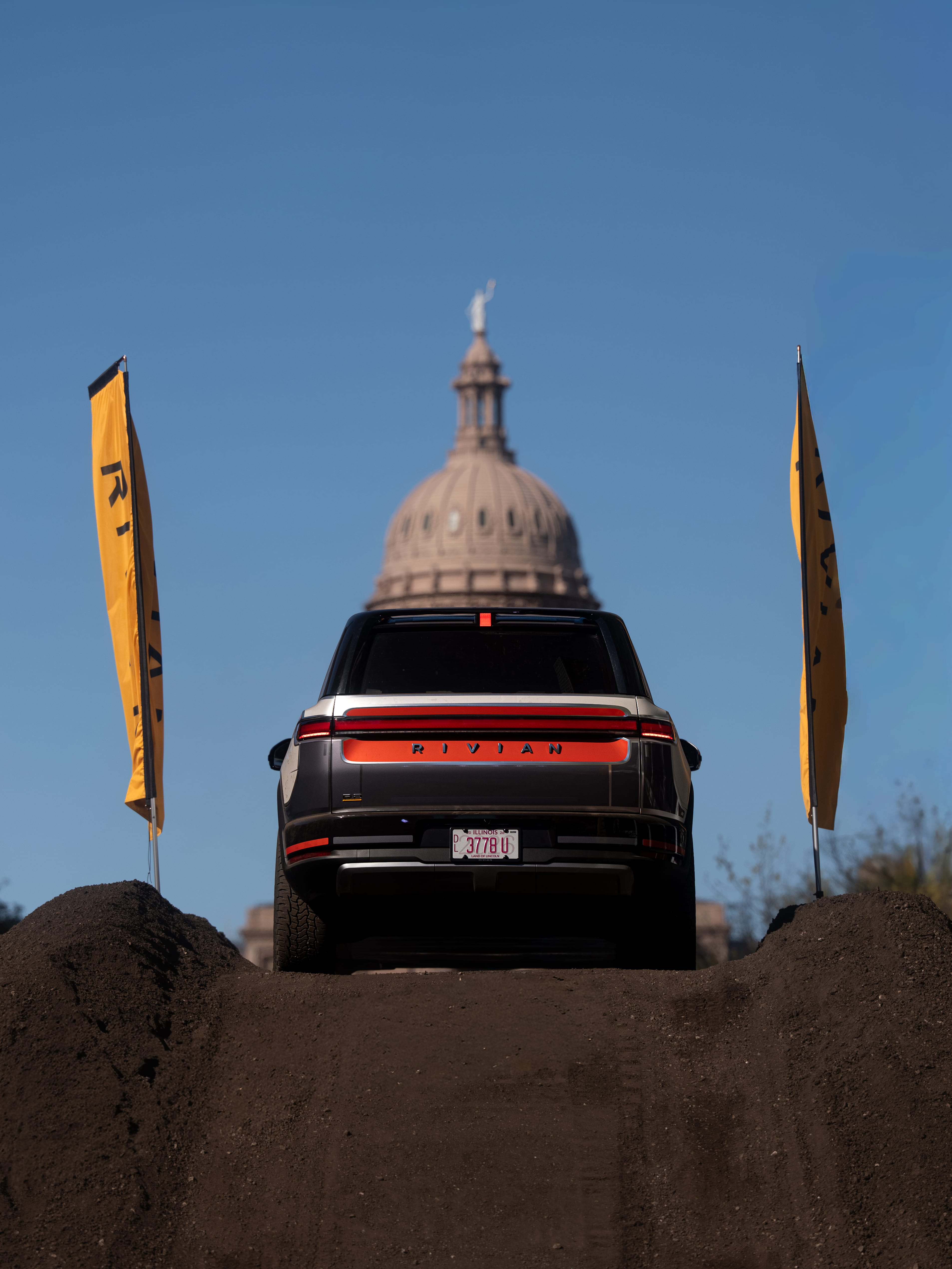 A Rivian R2 navigating a dirt course in Austin, Texas during SXSW 2026 with the State Capitol building blurred in the background.