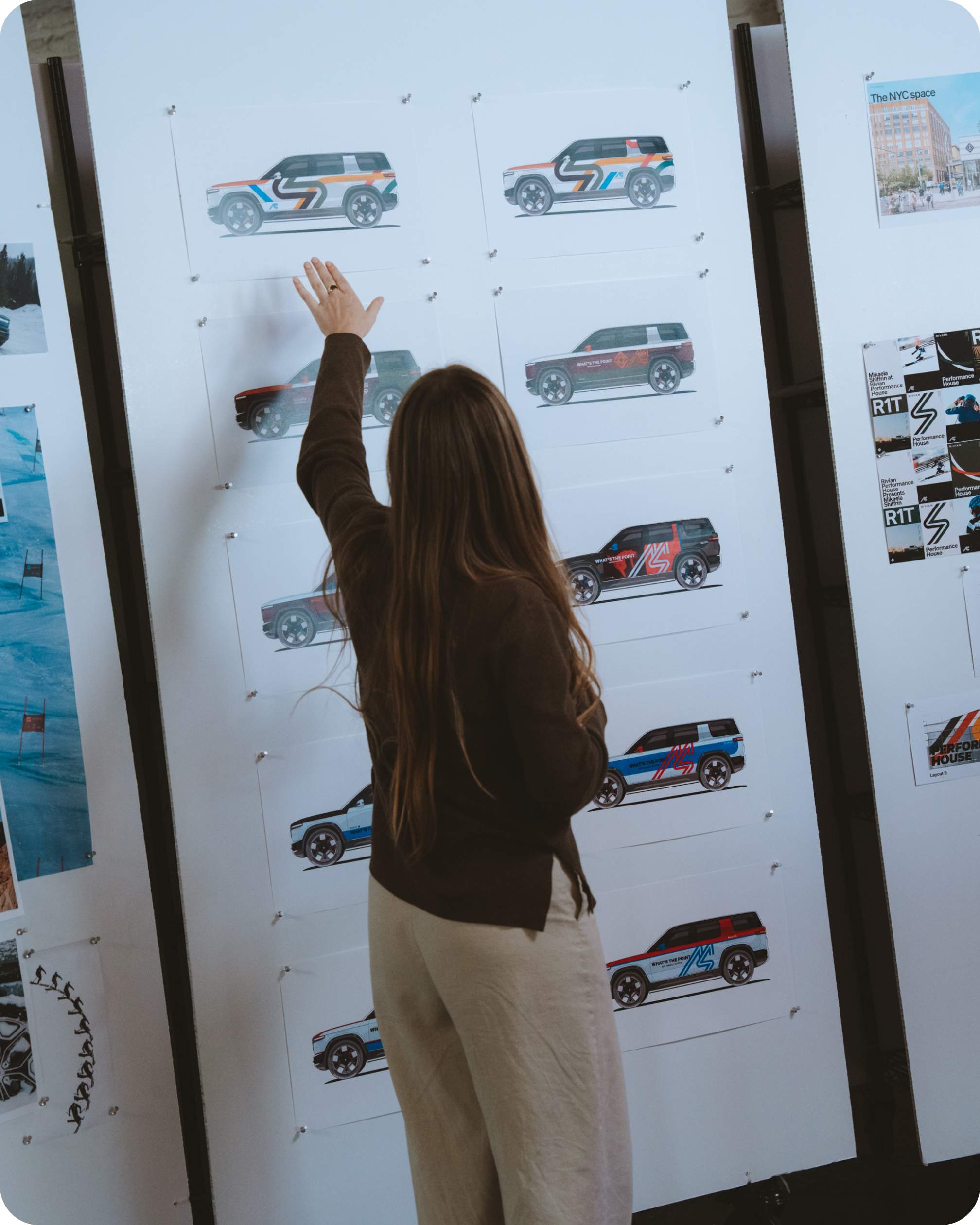 A producer standing in front of a big poster of vehicle mocks showing different custom color options of Rivian R1S electric SUVs. This is a behind the scenes shot of the development of the Performance House, in partnership with Mikaela Shiffrin.