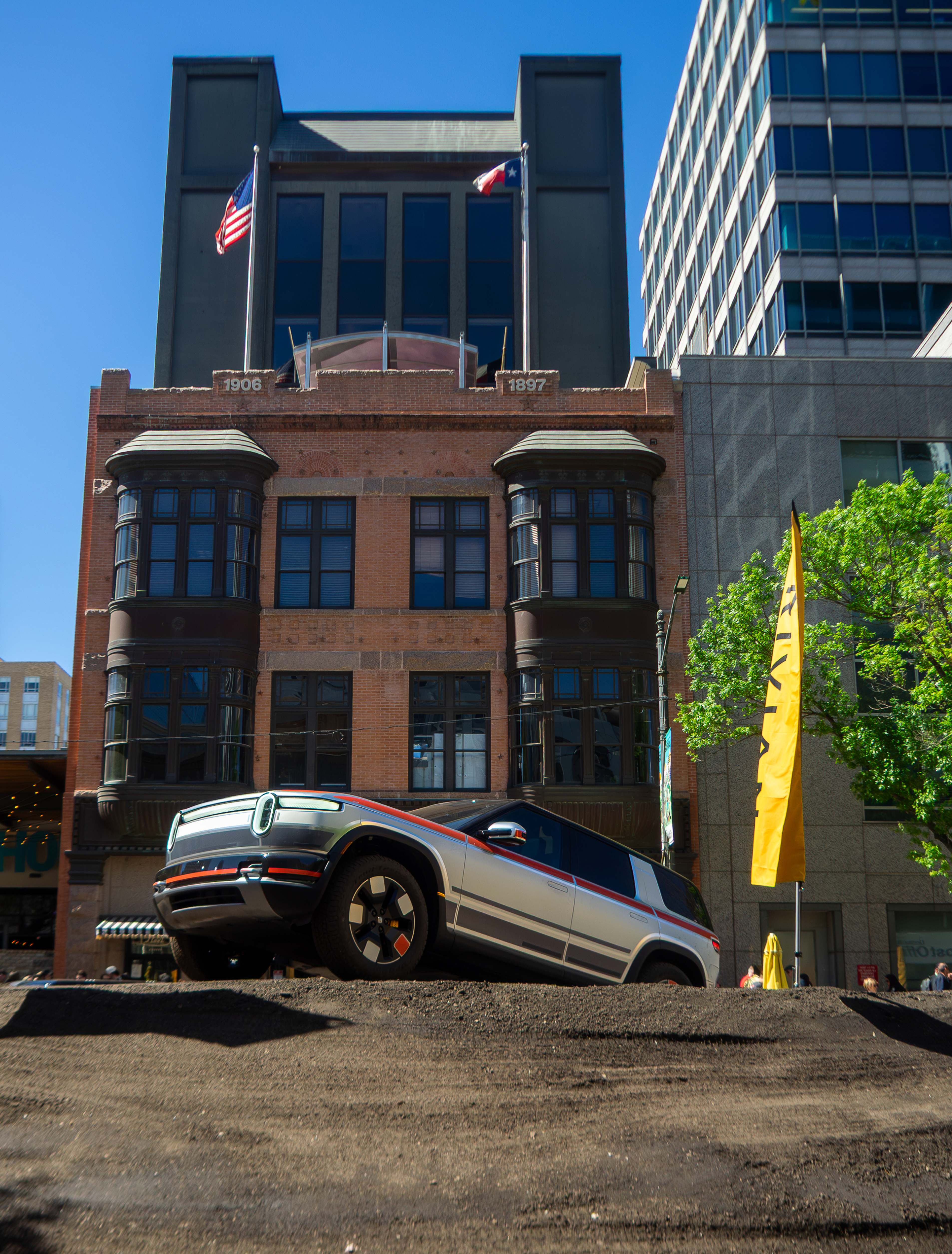 A Rivian R2 off-roading on a dirt course in front of historic architecture in downtown Austin during SXSW 2026.