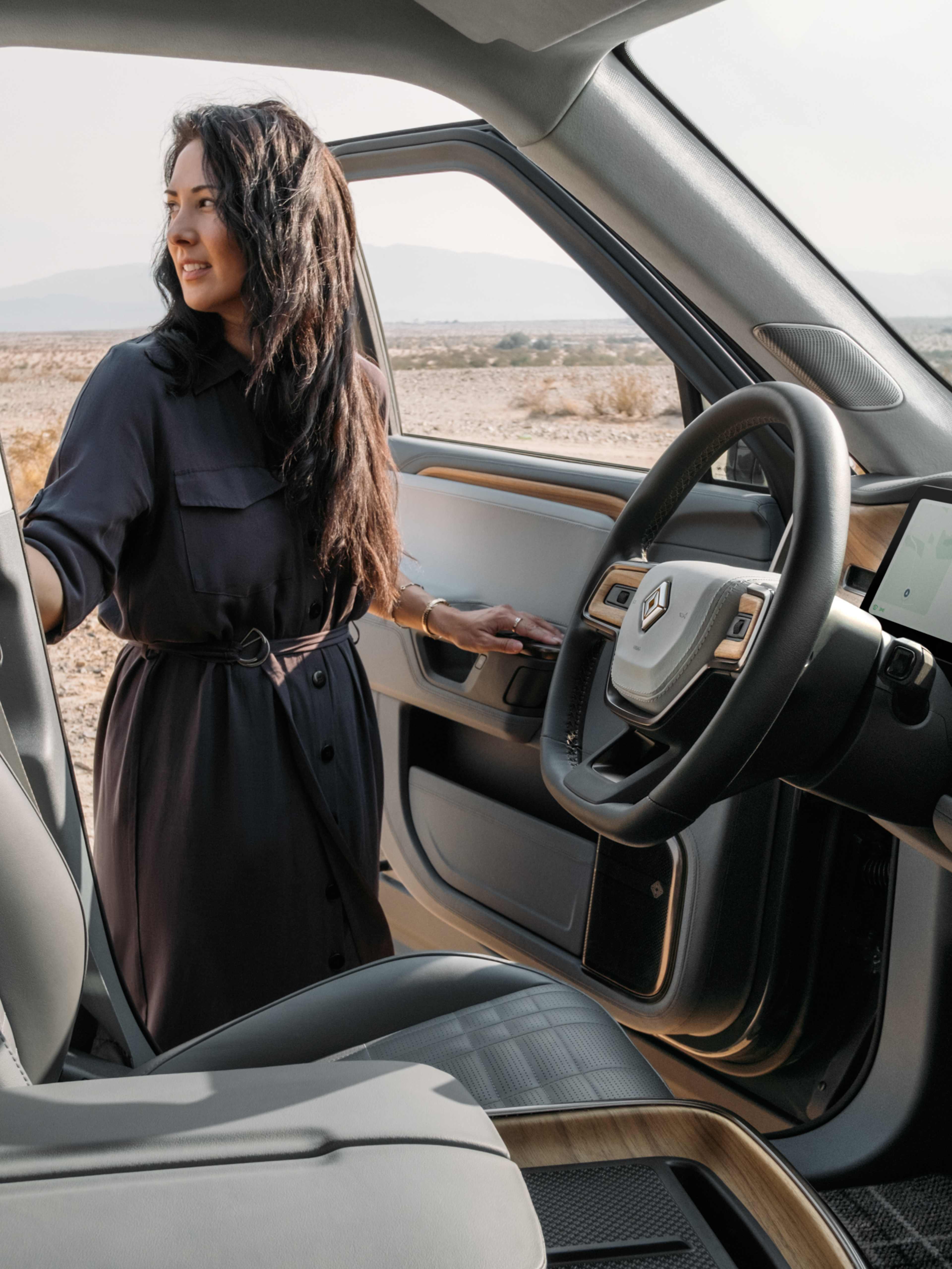 Une femme portant une robe foncée, debout près de la porte ouverte d'un VE Rivian.