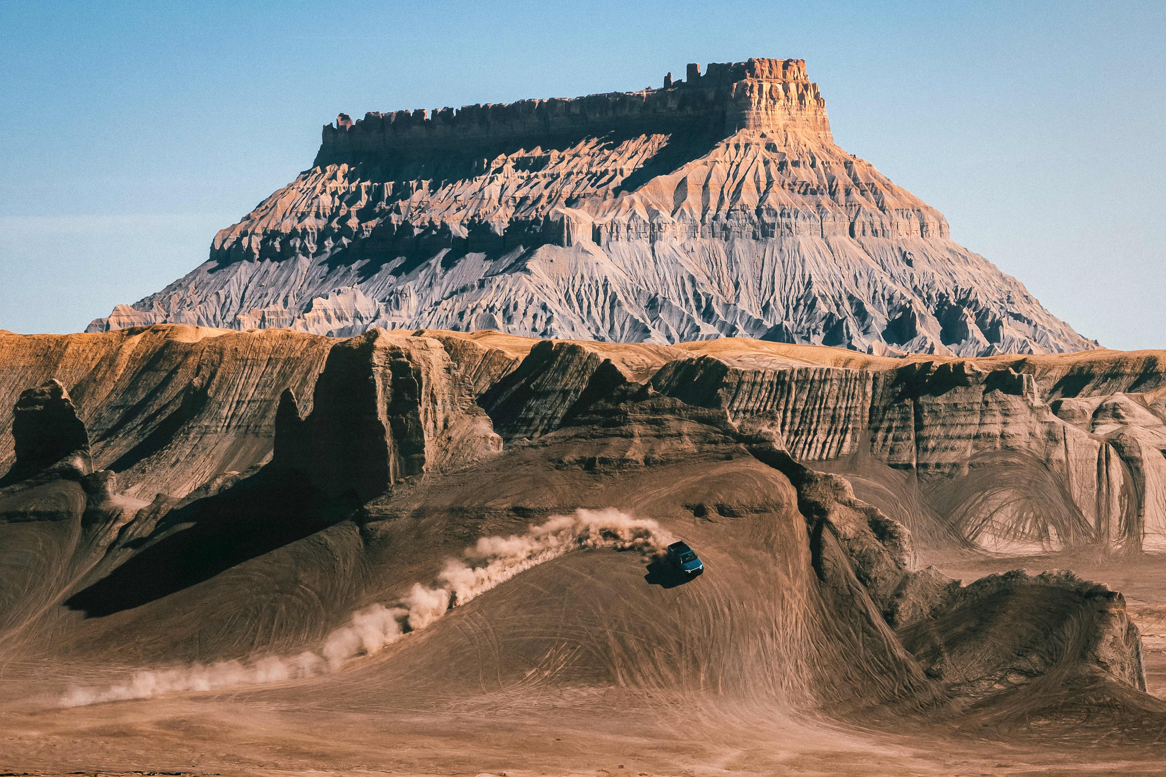 Un véhicule électrique Rivian effectuant un virage impressionnant sur le côté d'une falaise abrupte. Une traînée de poussière montre le chemin tracé par le virage.