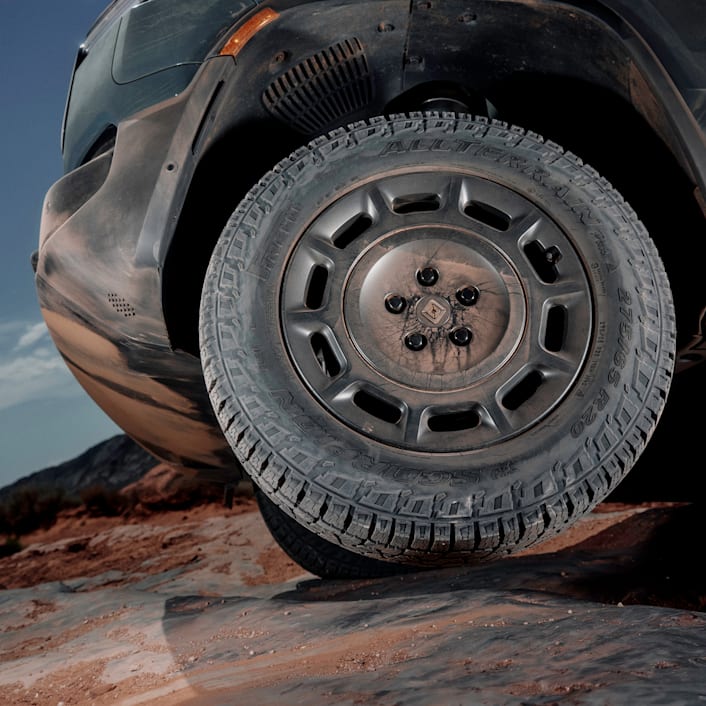 L'avant d'un véhicule électrique à quatre moteurs Rivian roulant sur une route sinueuse avec des falaises rougeâtres en arrière-plan. Le véhicule se déplace rapidement.