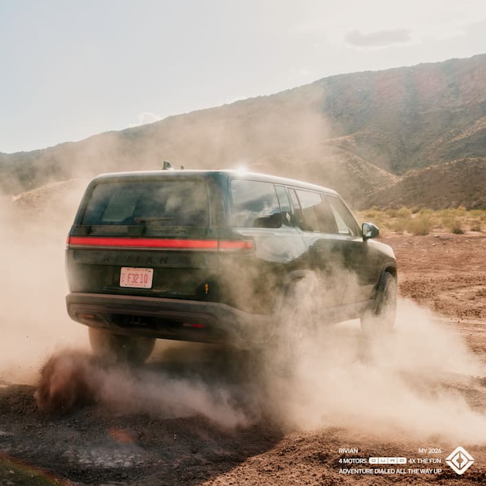 The back of a Rivian Quad motor electric SUV driving in a beautiful dirt valley. Dust kicks up and the vehicle turns.