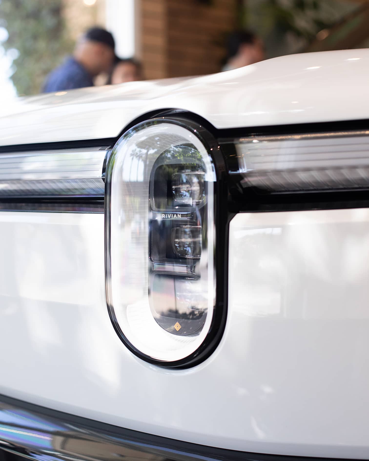 Close-up of the iconic vertical stadium headlight on a white SUV showcased at a Rivian R2 Block Party.