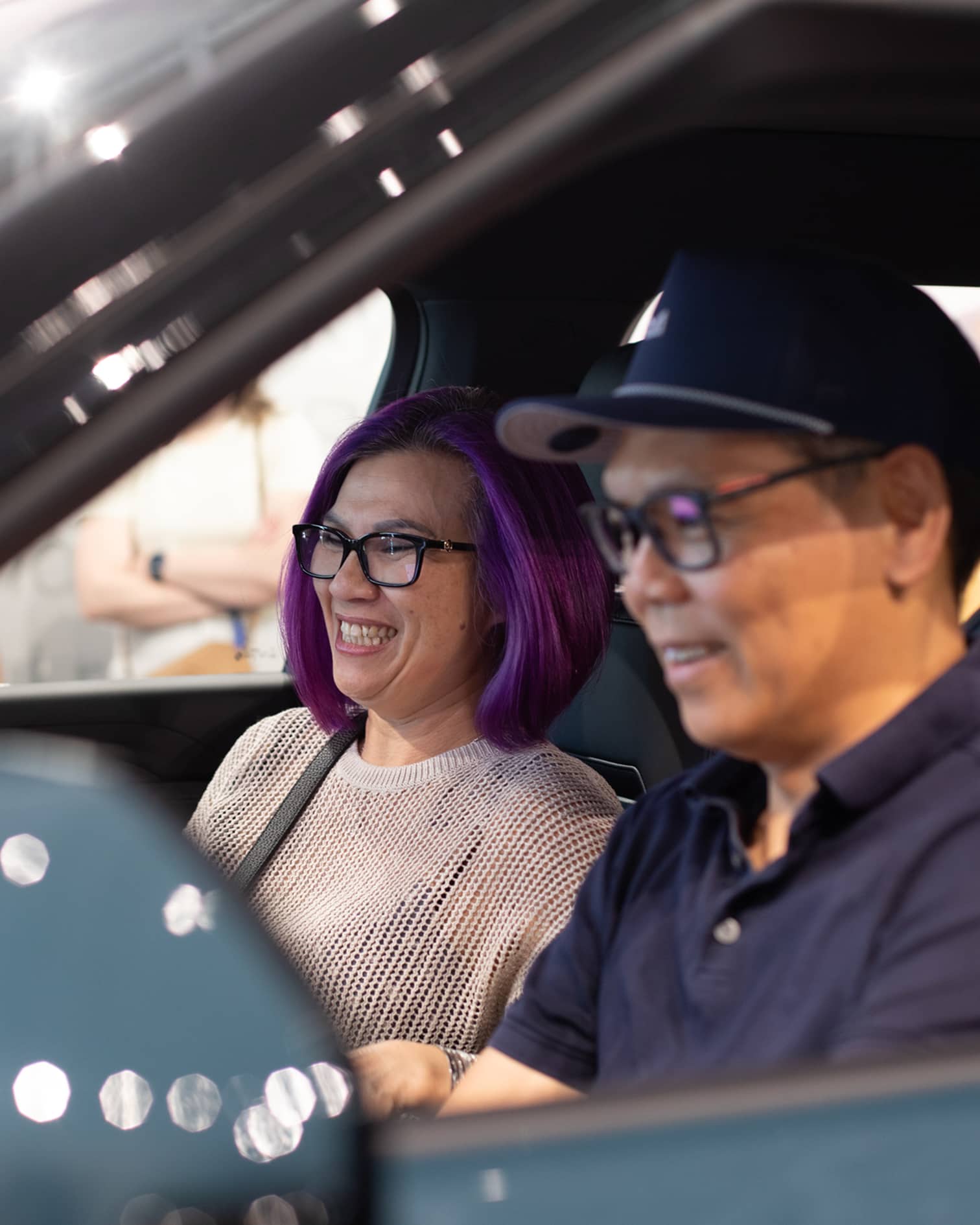 A smiling woman and man sit inside a new electric vehicle at a Rivian R2 Block Party.