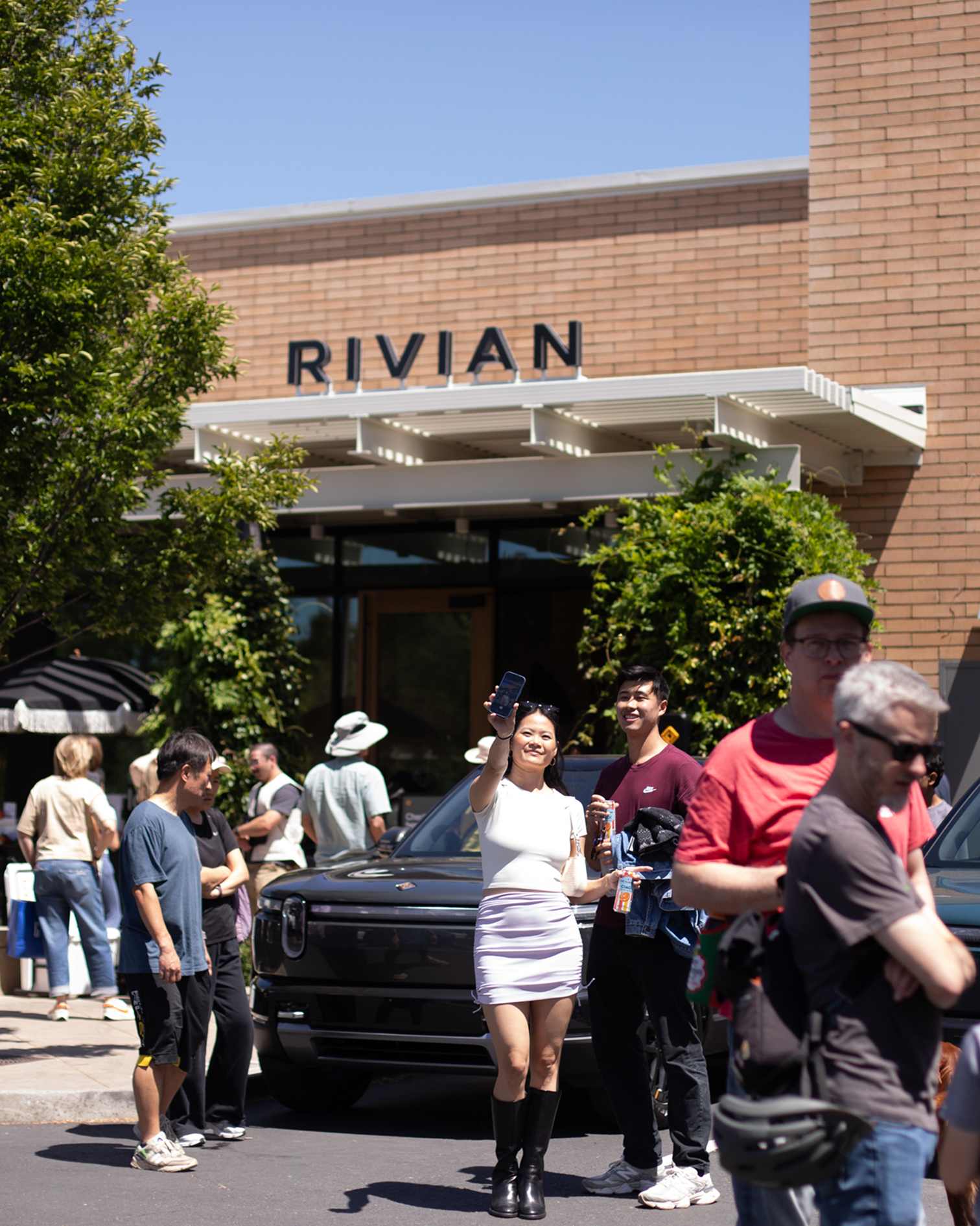 Attendees mingle and a woman takes a selfie in front of a showroom entrance during a Rivian R2 Block Party.