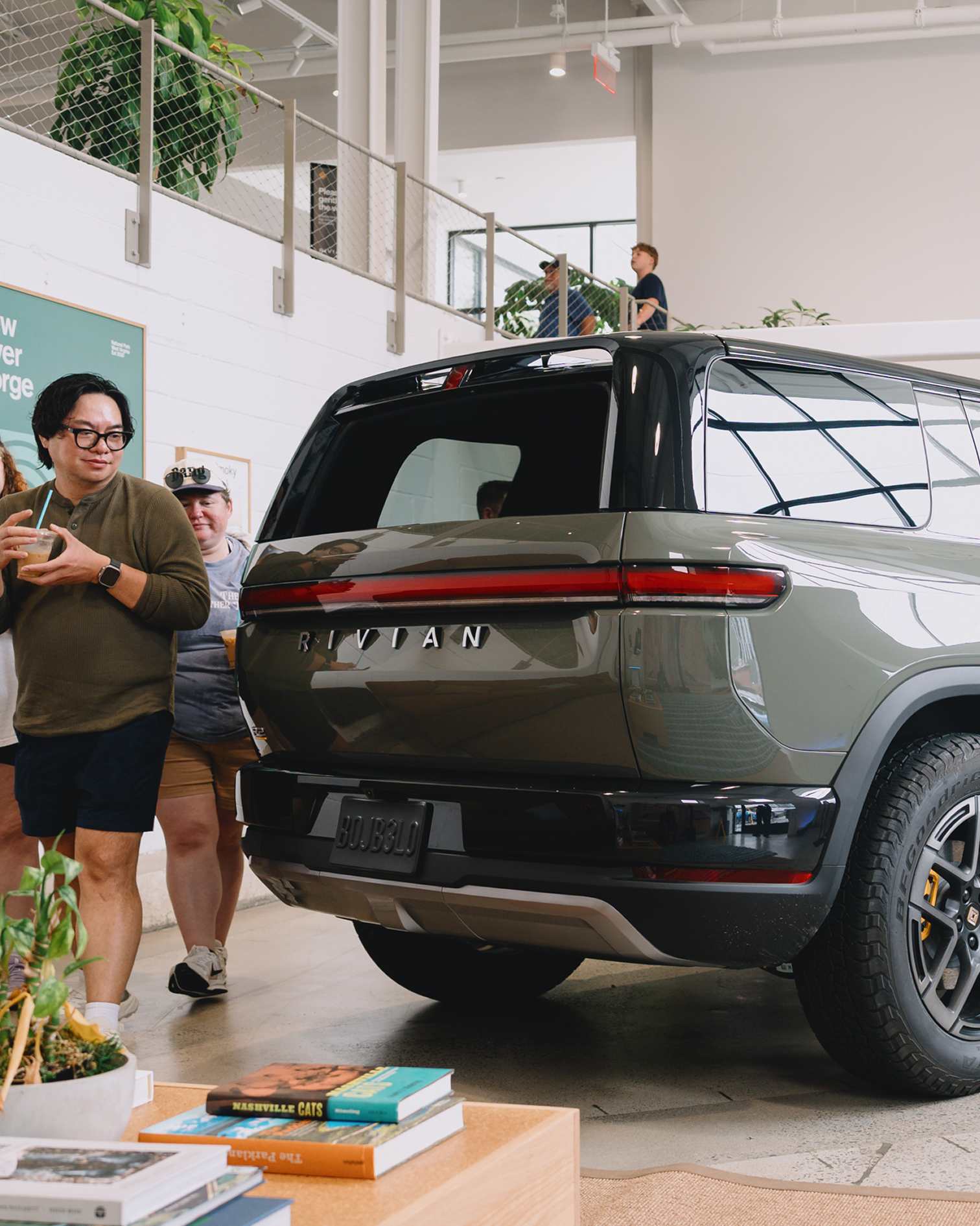 Guests admire the rear design of a glossy green R2 electric SUV displayed inside a showroom at a Rivian R2 Block Party.