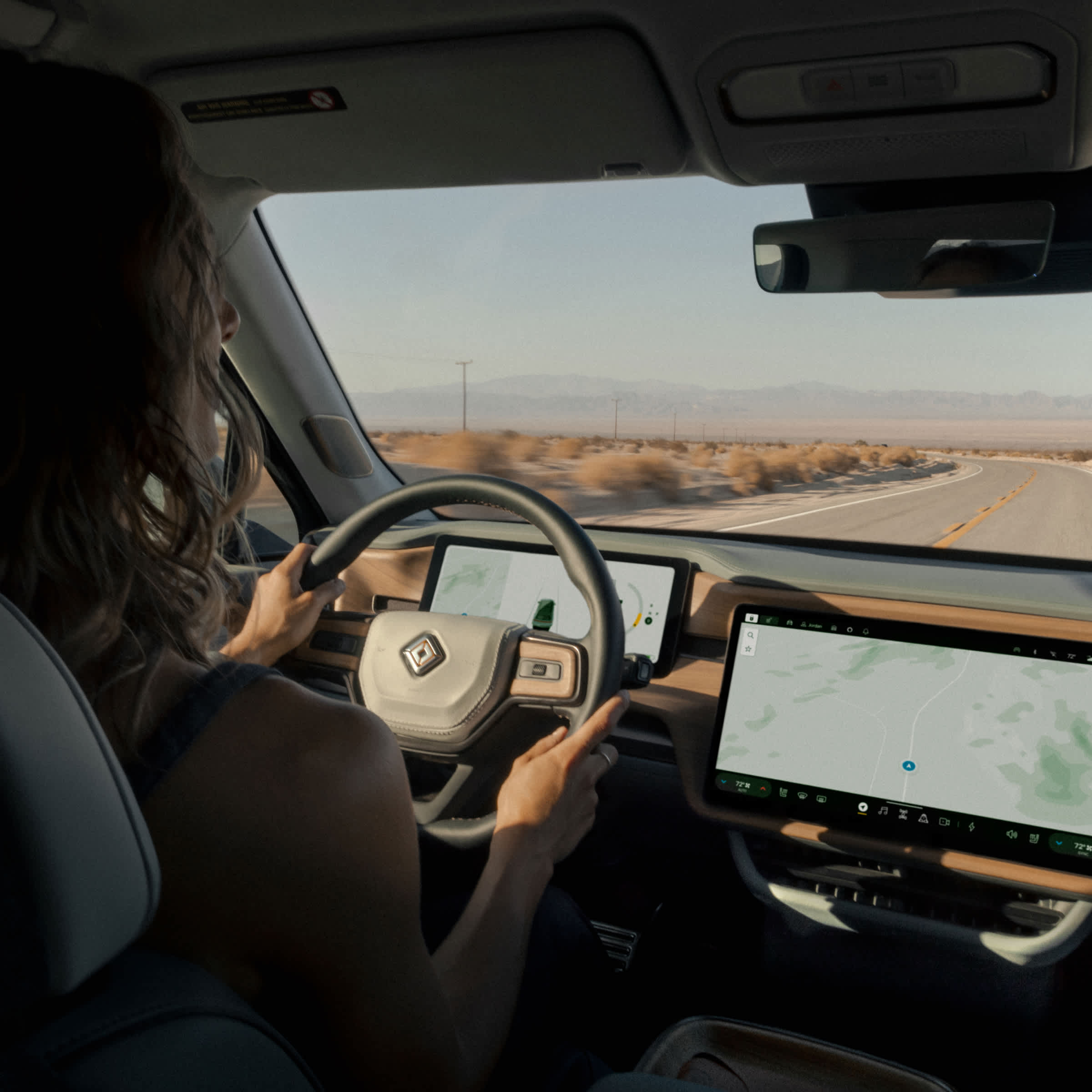 From the perspective of a backseat passenger, an over the shoulder view of a person driving a Rivian electric vehicle on an open highway.