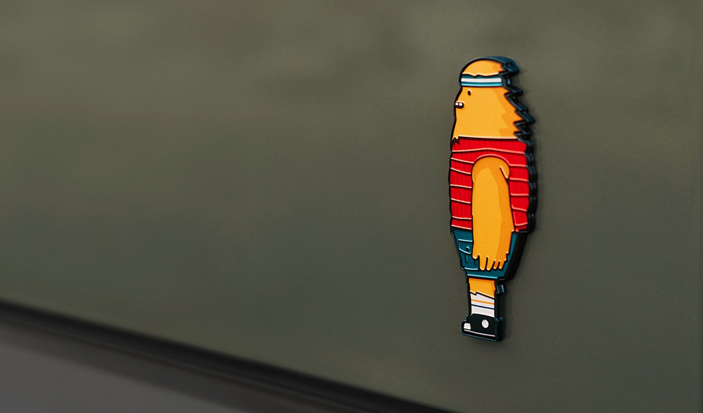 The rear truck badging of a Rivian Quad motor electric vehicle. The badge depicts the Rivian Gear Guard friendly monster character, with wind blowing through their hair.