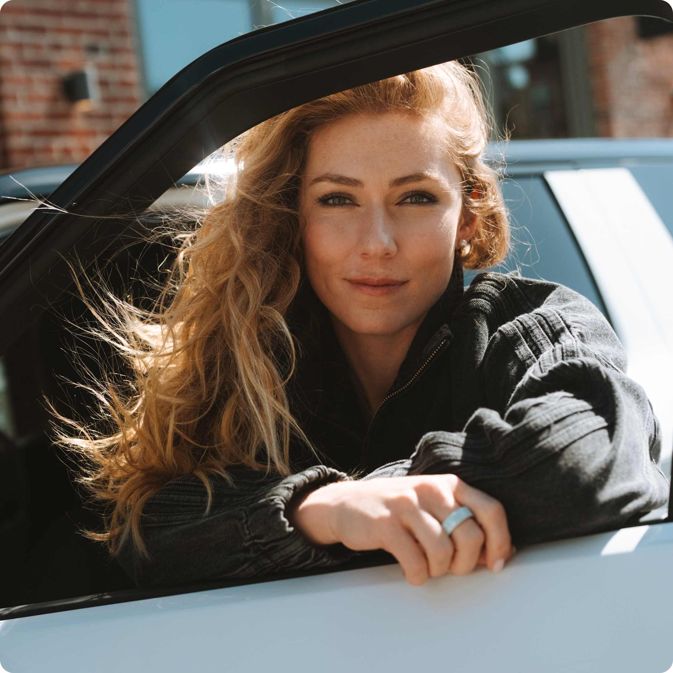 Mikaela Shiffrin leaning against the open driver door of a Rivian electric vehicle.