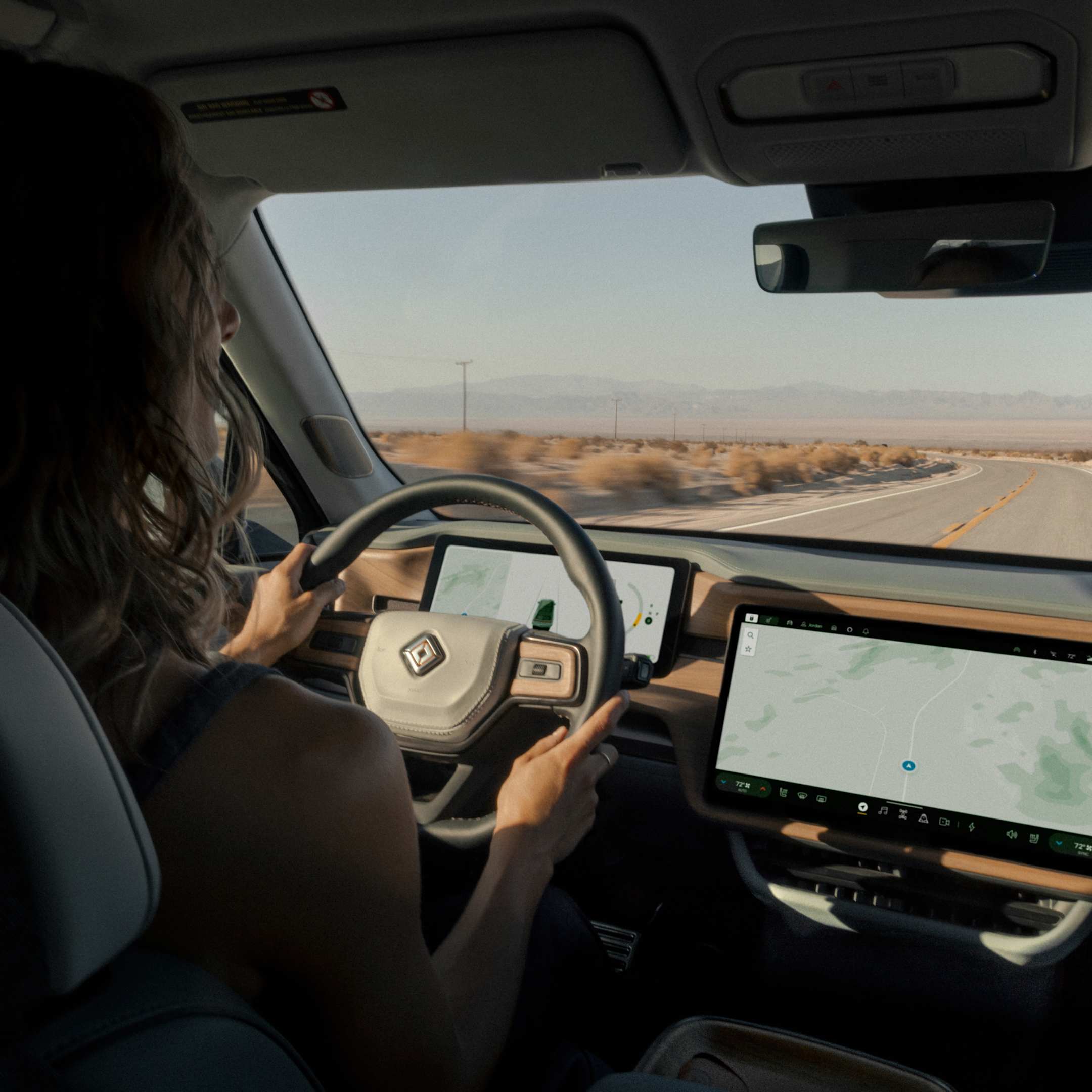 From the perspective of a backseat passenger, an over the shoulder view of a person driving a Rivian electric vehicle on an open highway.