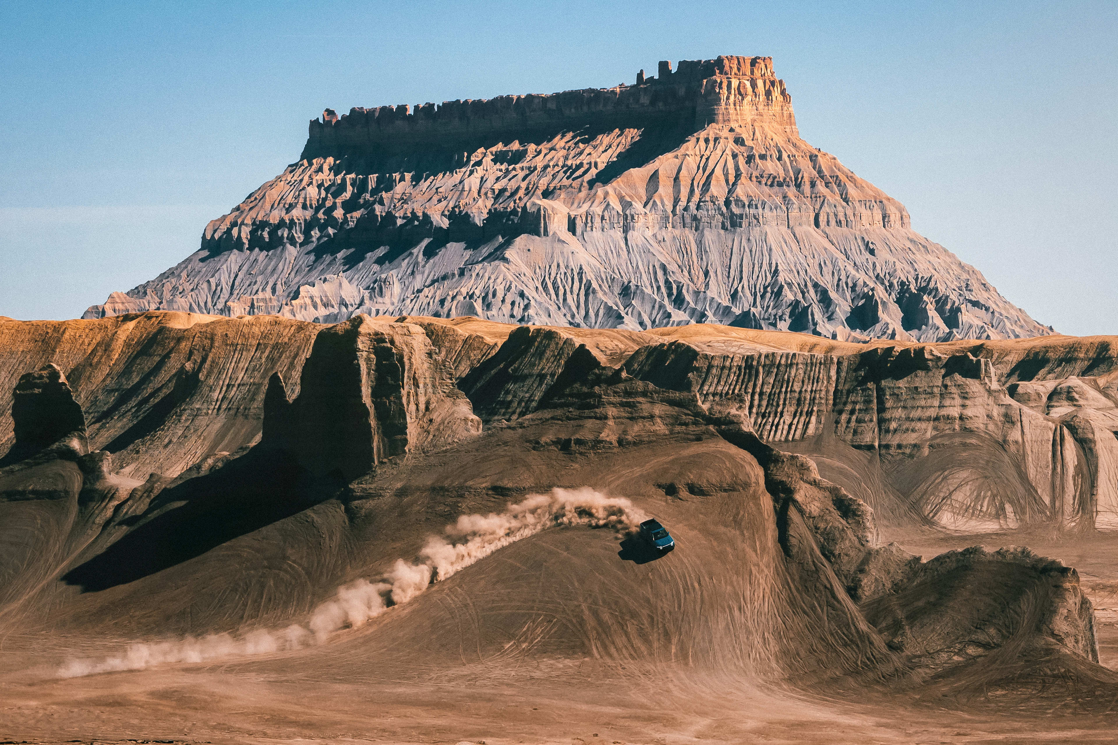 A Rivian electric vehicle performing an impressive turn up the side of a steep cliff. A trail of dust shows the path of the cliff turn.