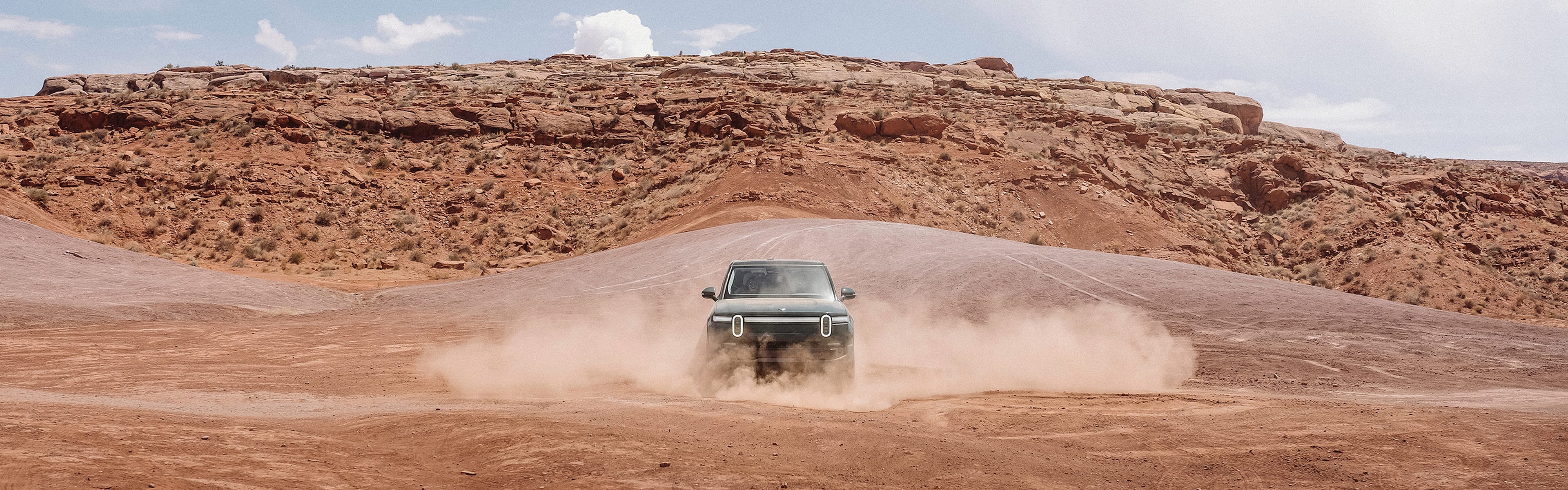 A Rivian electric vehicle performing turns and kicking up dust in a dirt valley.