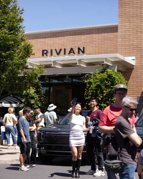Attendees mingle and a woman takes a selfie in front of a showroom entrance during a Rivian R2 Block Party.