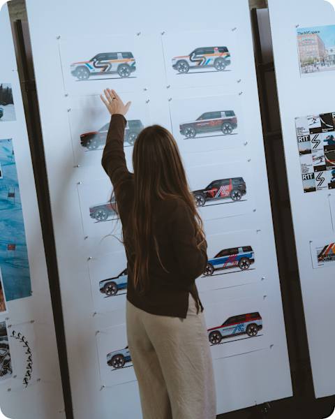 A producer standing in front of a big poster of vehicle mocks showing different custom color options of Rivian R1S electric SUVs. This is a behind the scenes shot of the development of the Performance House, in partnership with Mikaela Shiffrin.