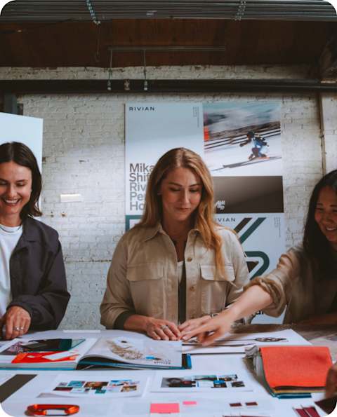 Mikaela Shiffrin and two producers standing in front of a table, reviewing blueprints and color swatches for the Performance House. Mikaela is standing in the middle.