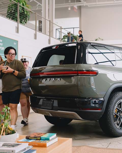 Guests admire the rear design of a glossy green R2 electric SUV displayed inside a showroom at a Rivian R2 Block Party.