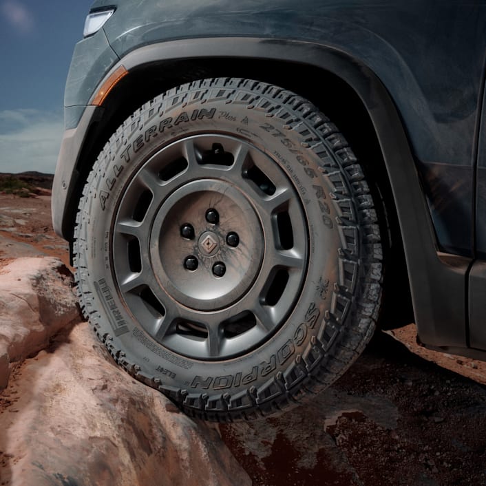 An action shot from a low point-of-view of the front driver side wheel. The wheel features rugged tires and 20” Dune Satin Graphite All-Terrain wheels. 