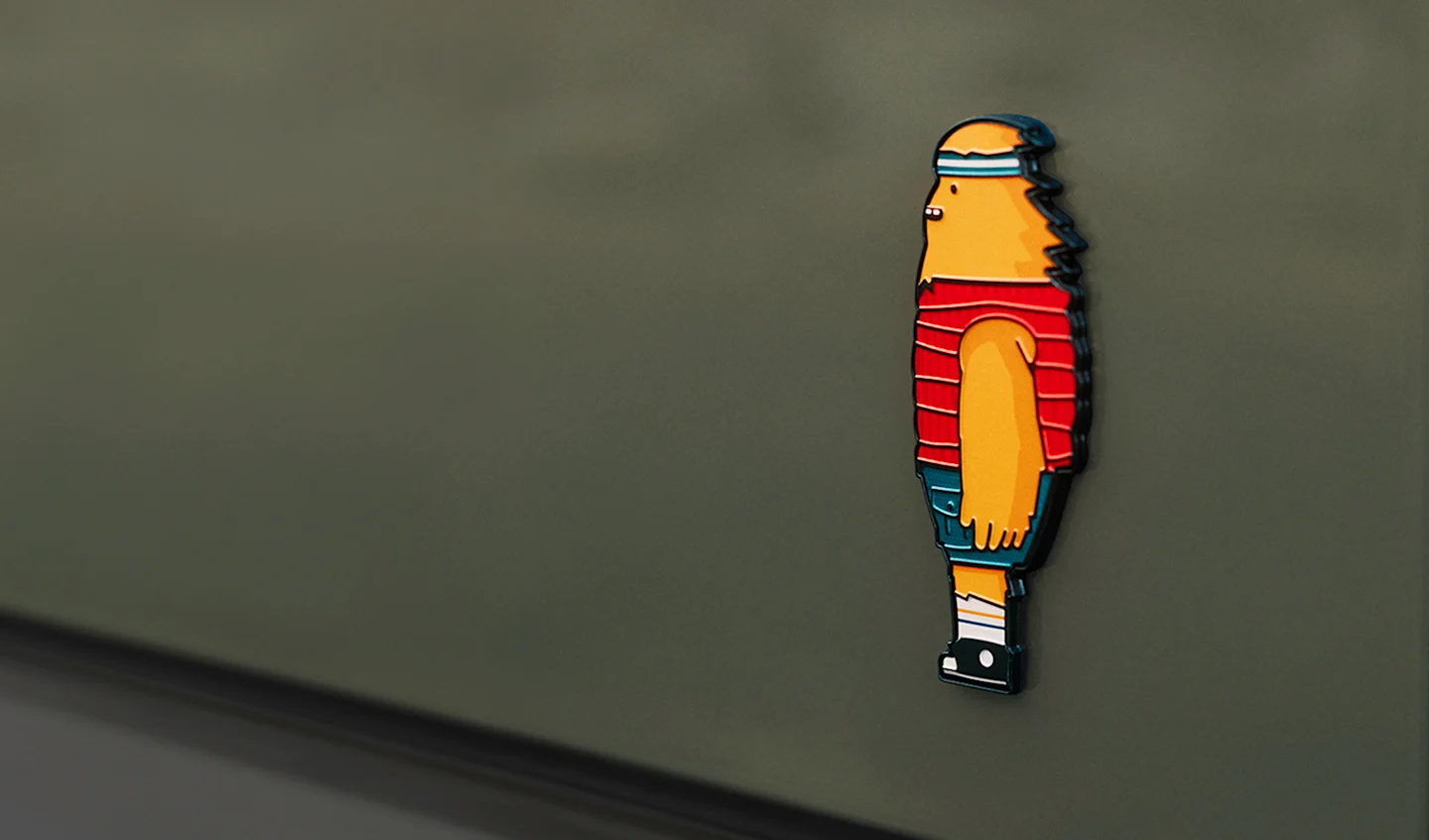 The rear truck badging of a Rivian Quad motor electric vehicle. The badge depicts the Rivian Gear Guard friendly monster character, with wind blowing through their hair.