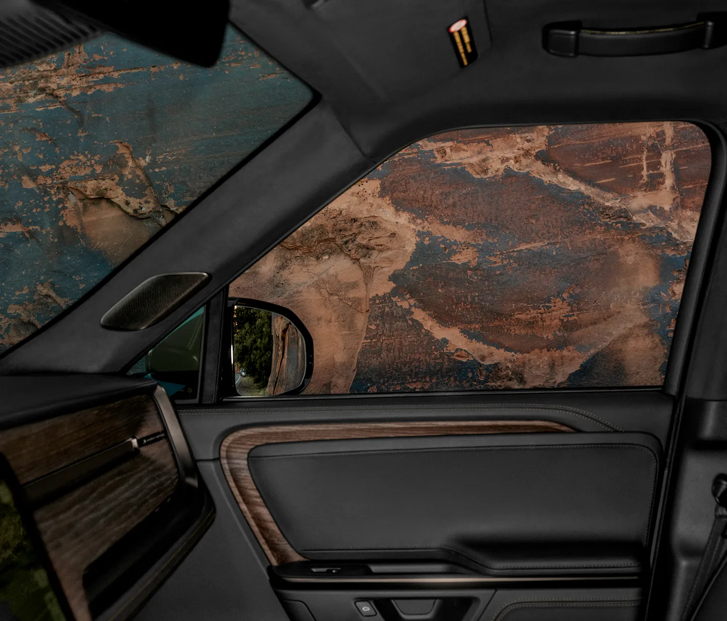 The interior of a Rivian Quad motor electric vehicle. The interior has luxurious dark upholstery with wood trim. 