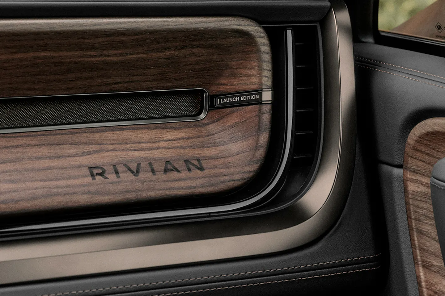An interior view of the passenger glove box of a Rivian electric vehicle. The passenger glove compartment and dashboard are lined with black leather and features dark wood accents.