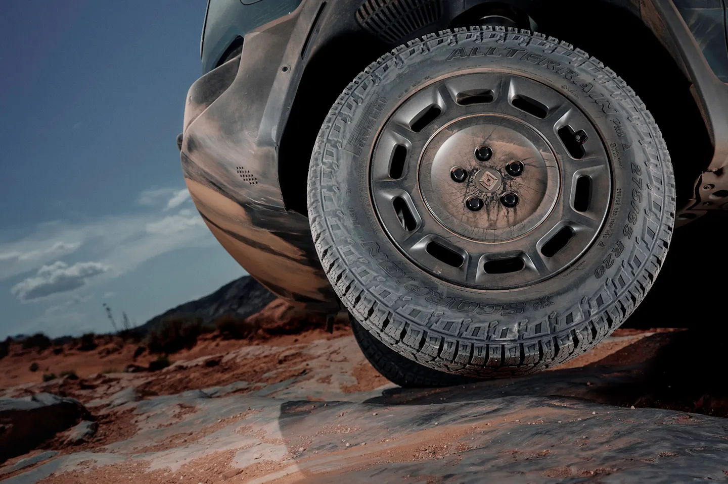 An action shot from a low point-of-view of the front driver side wheel. The wheel features rugged tires and 20” Dune Satin Graphite All-Terrain wheels. 