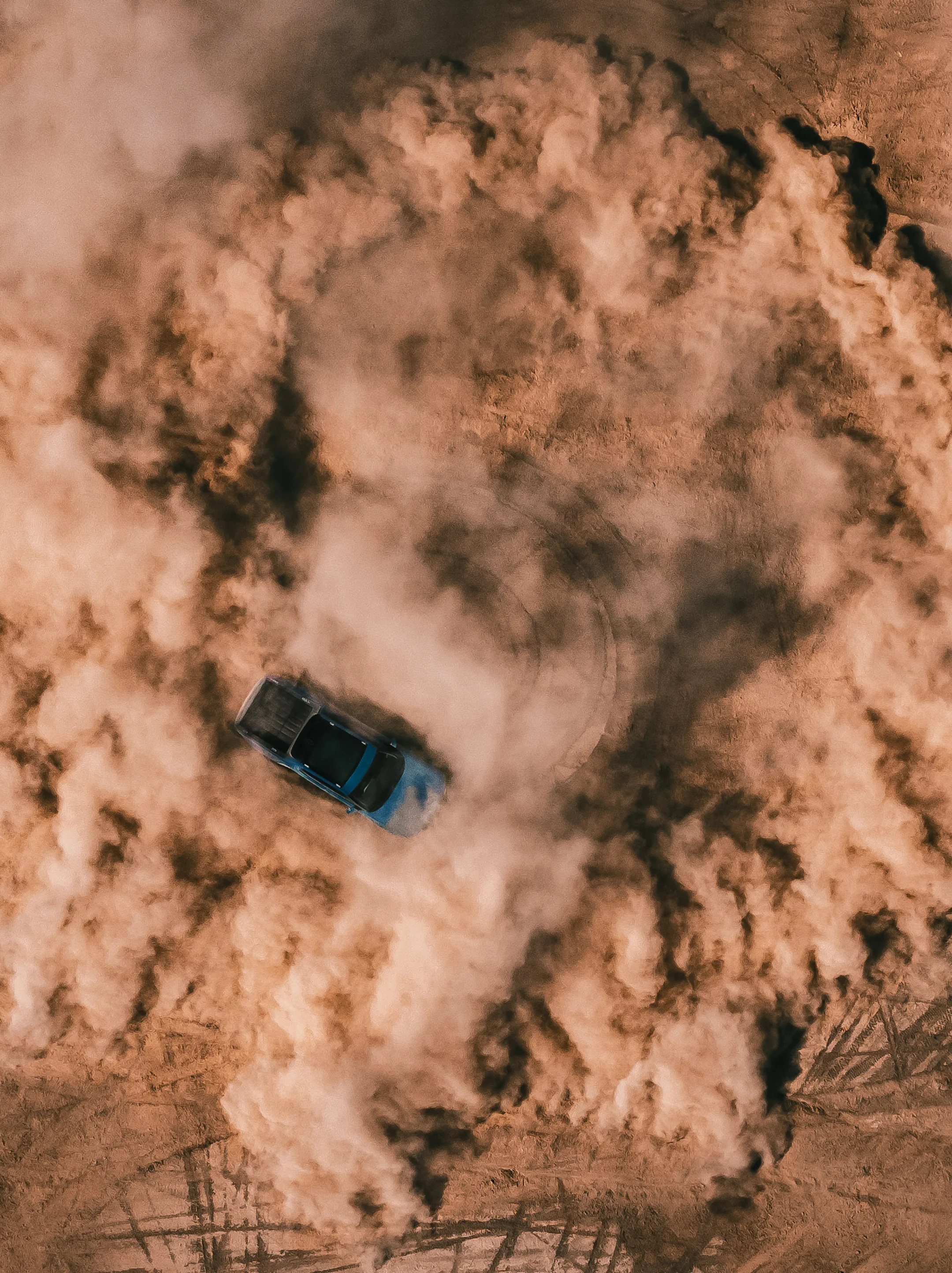 An aerial shot of a Rivian Quad motor electric vehicle utilizing 4 motor vectoring to perform a tight, controlled, circular spin on a dirt landscape. Dust fills the air and circular tire marks line the ground.