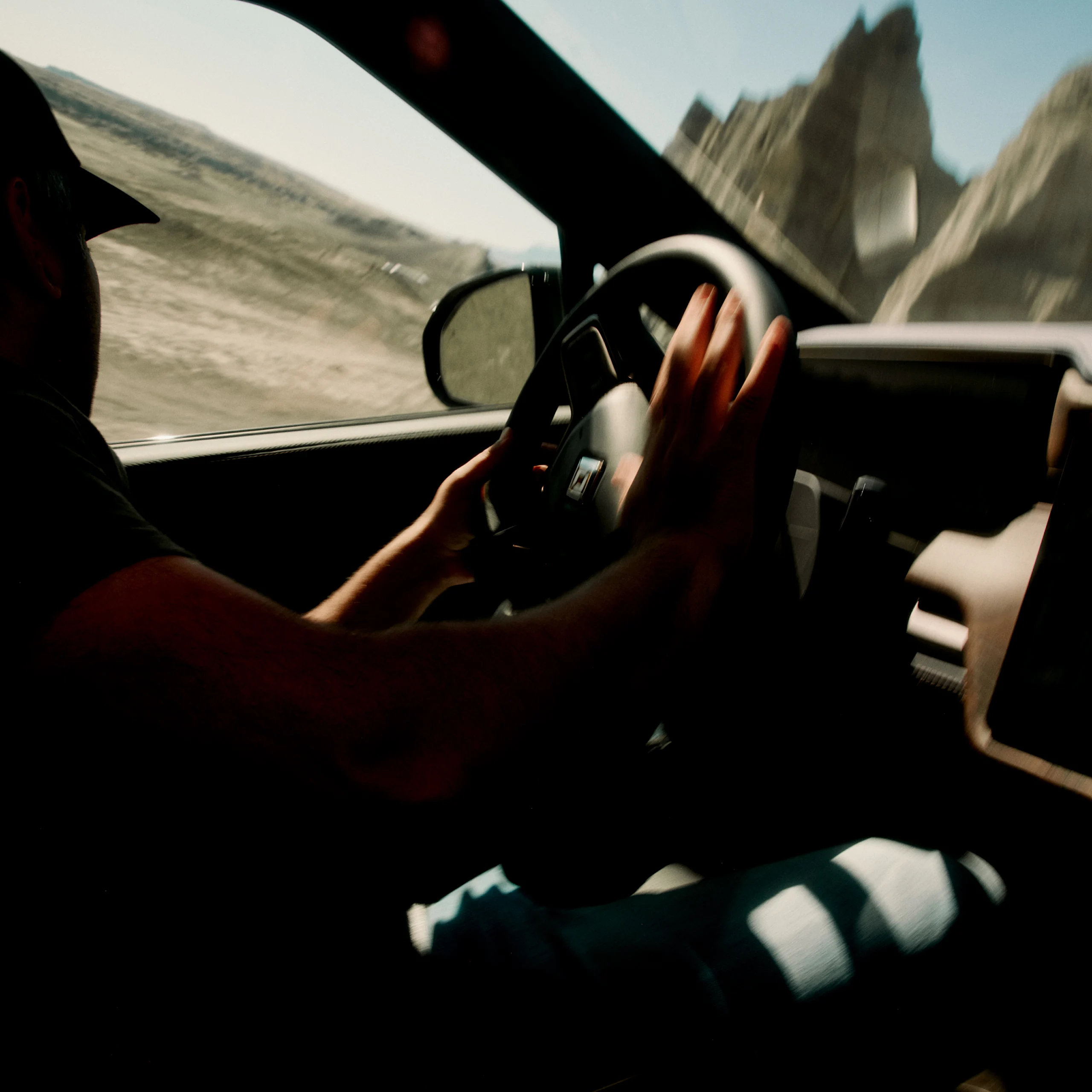 An interior shot of the driver position inside a Rivian Quad motor electric vehicle. The diver is turning the wheel as the car swiftly moves up the side of a large hill.