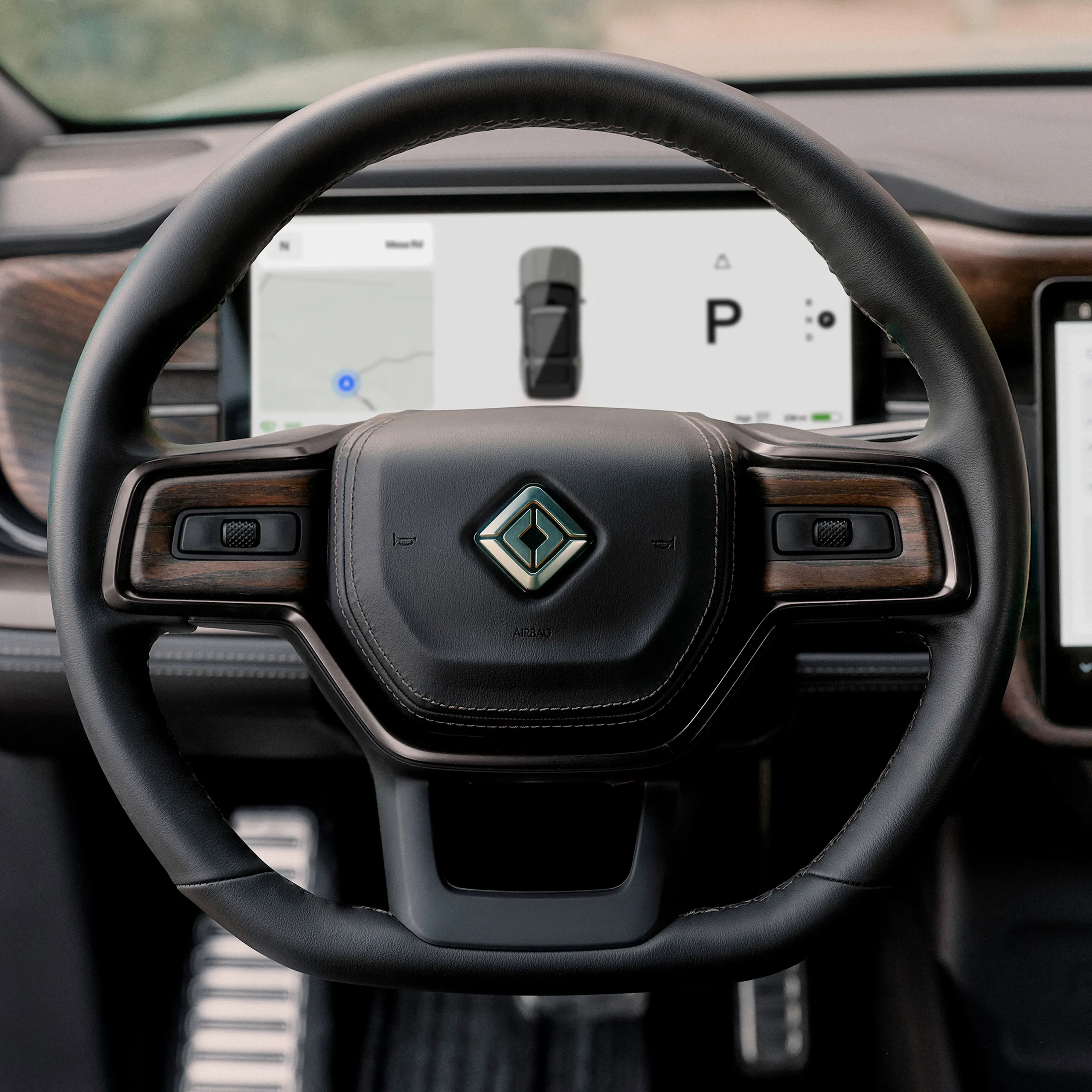 The steering wheel and odometer screen of a Rivian electric vehicle. The black leather steering wheel is trimmed with dark wood accents.