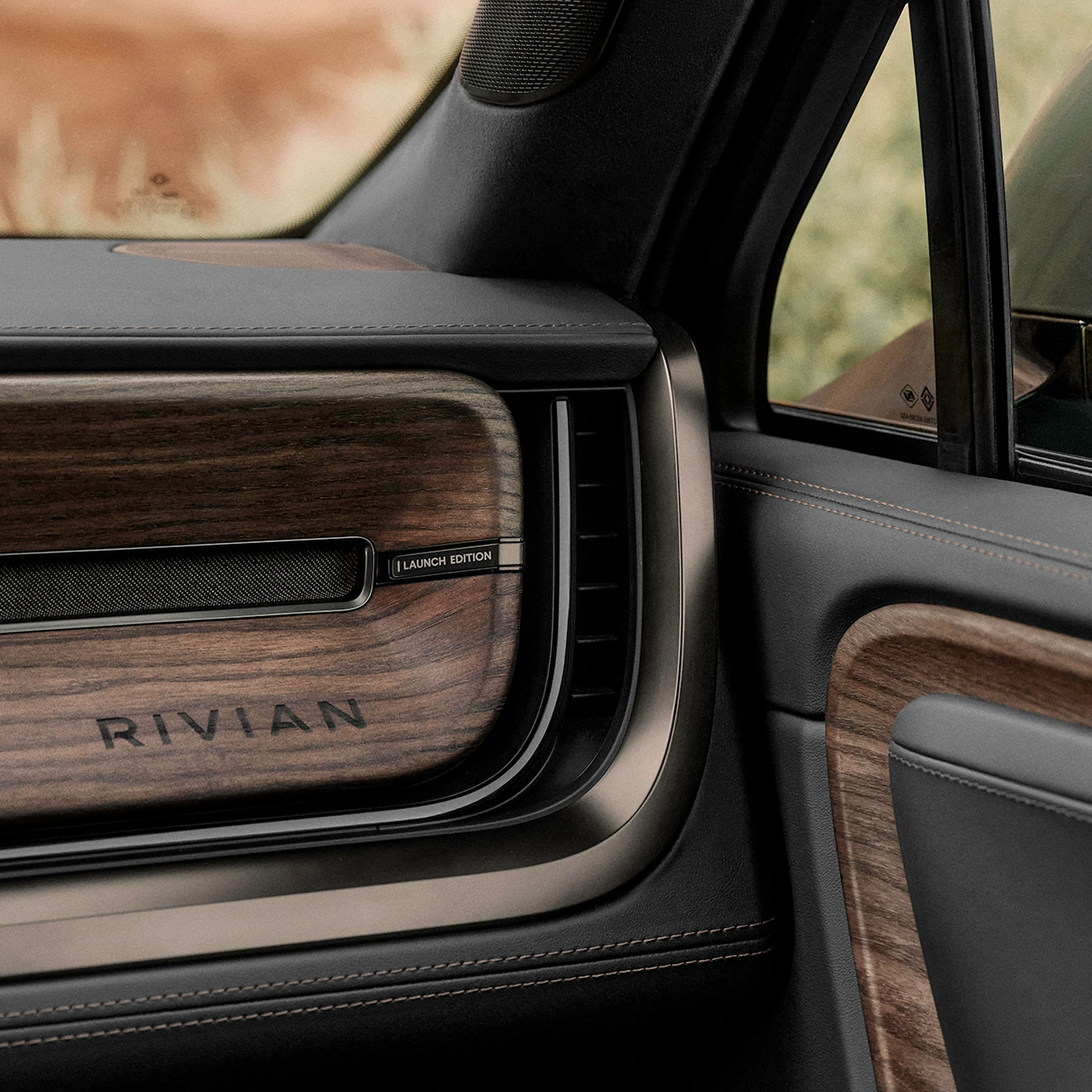 An interior view of the passenger glove box of a Rivian electric vehicle. The passenger glove compartment and dashboard are lined with black leather and features dark wood accents.