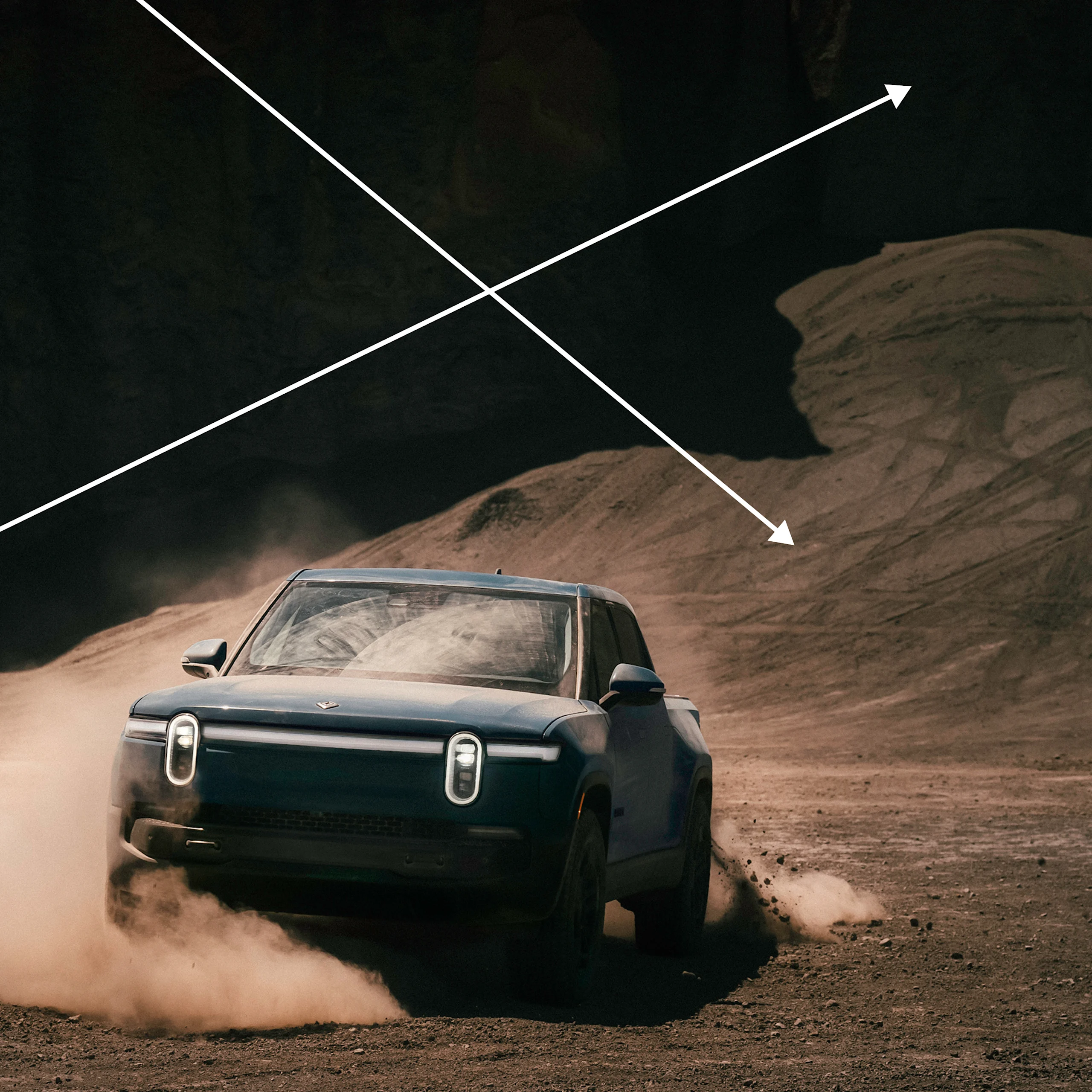 The front of a Rivian R1T EV truck drifting a turn in a dusty dirt valley.