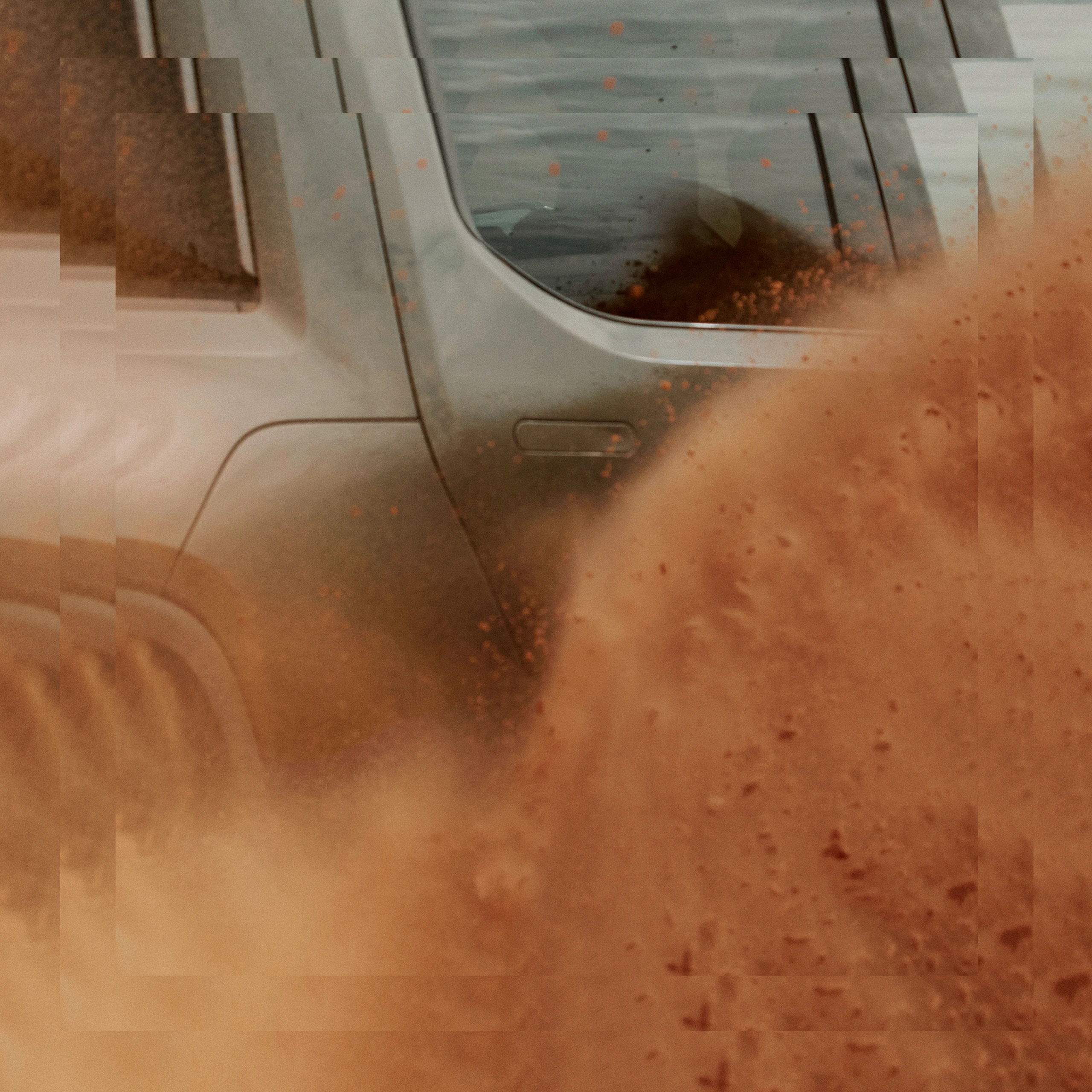 A stylized close up shot of the passenger side of a Rivian R1T electric vehicle kicking a very heavy plume of red dust.