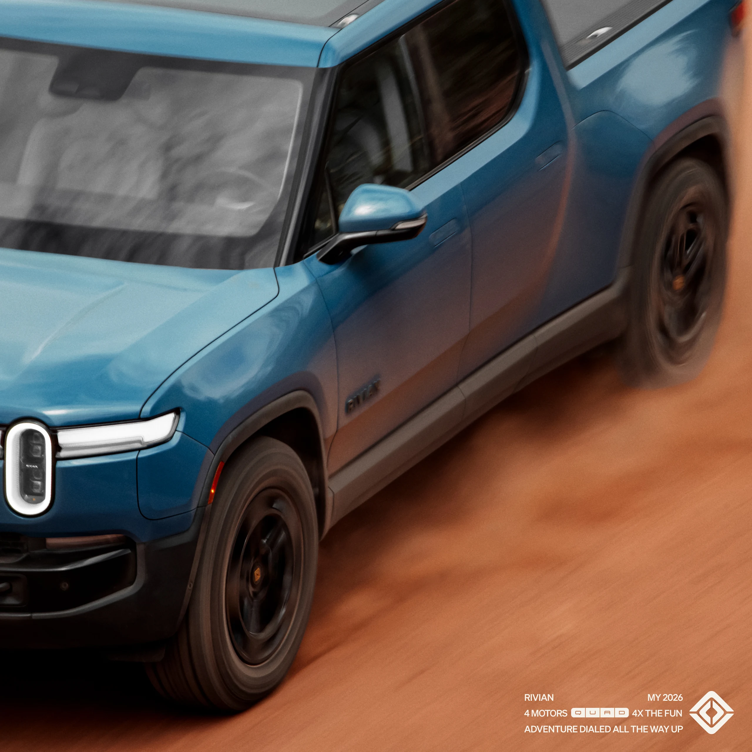 A top view shot of a blue Rivian EV truck driving quickly across red dirt road.