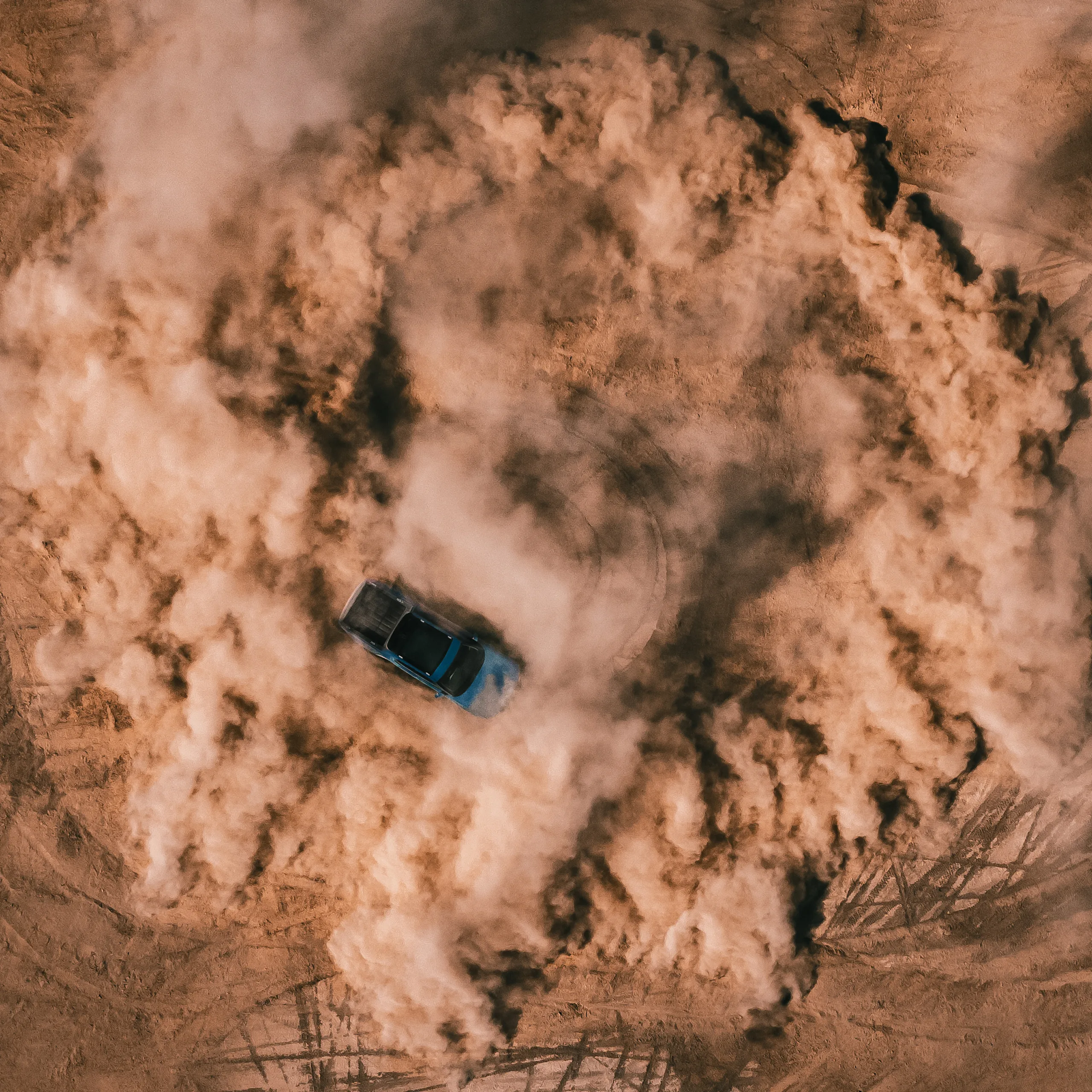 An aerial shot of a Rivian Quad motor electric vehicle utilizing 4 motor vectoring to perform a tight, controlled, circular spin on a dirt landscape. Dust fills the air and circular tire marks line the ground.