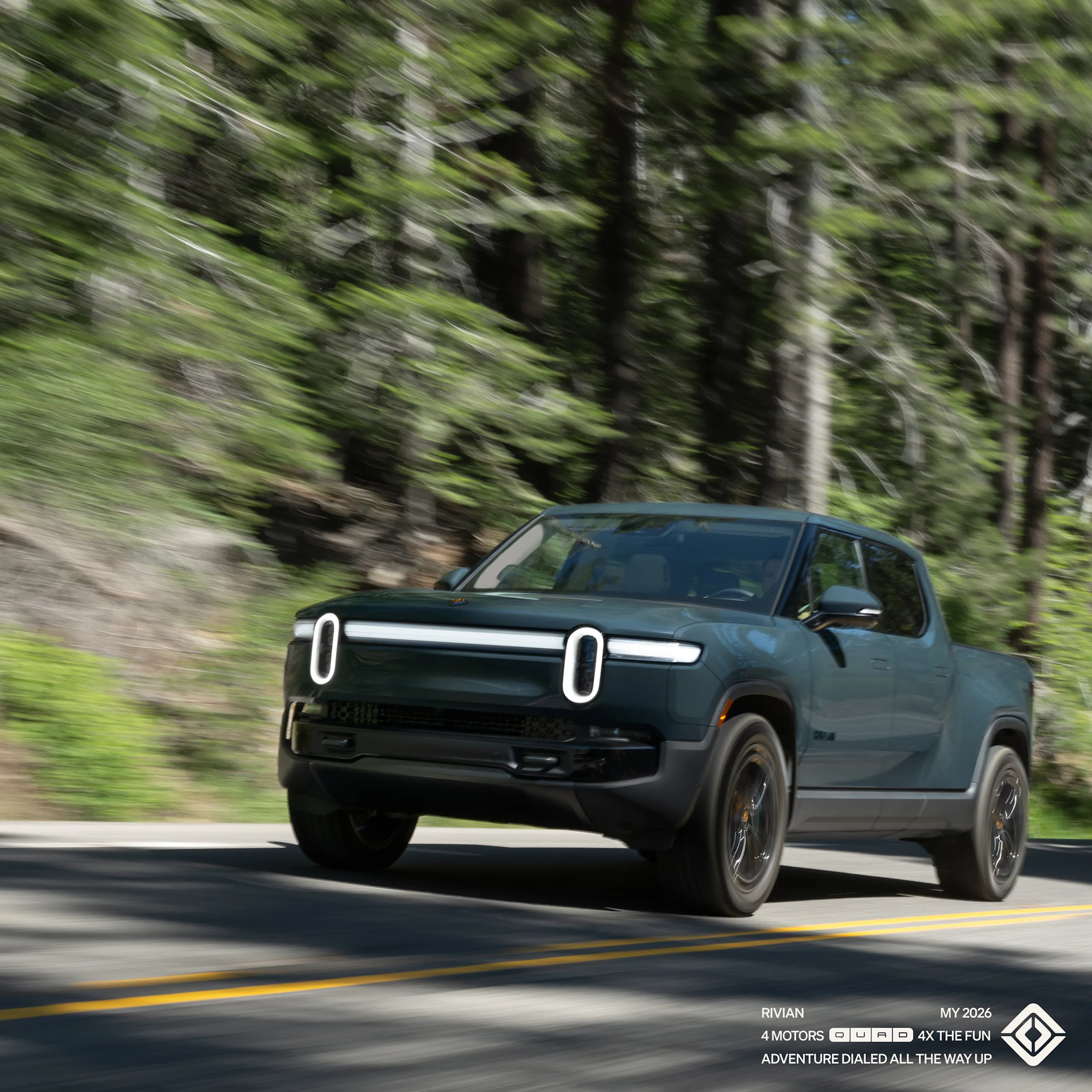 A Rivian R1T electric truck driving on a two lane highway with green bushes and trees in the background. The car features Storm Blue paint, and Laguna Blue accents exclusive to Rivian Quad motor trims.