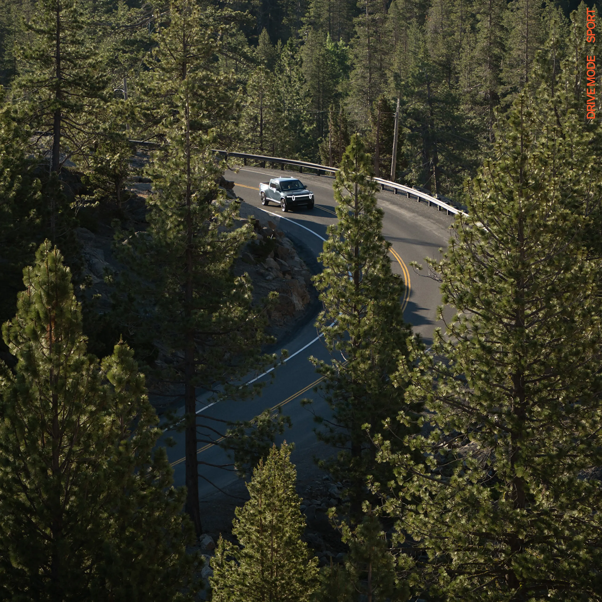 An aerial shot of a R1T electric truck driving down a winding highway, cutting through a dense expanse of pine trees.