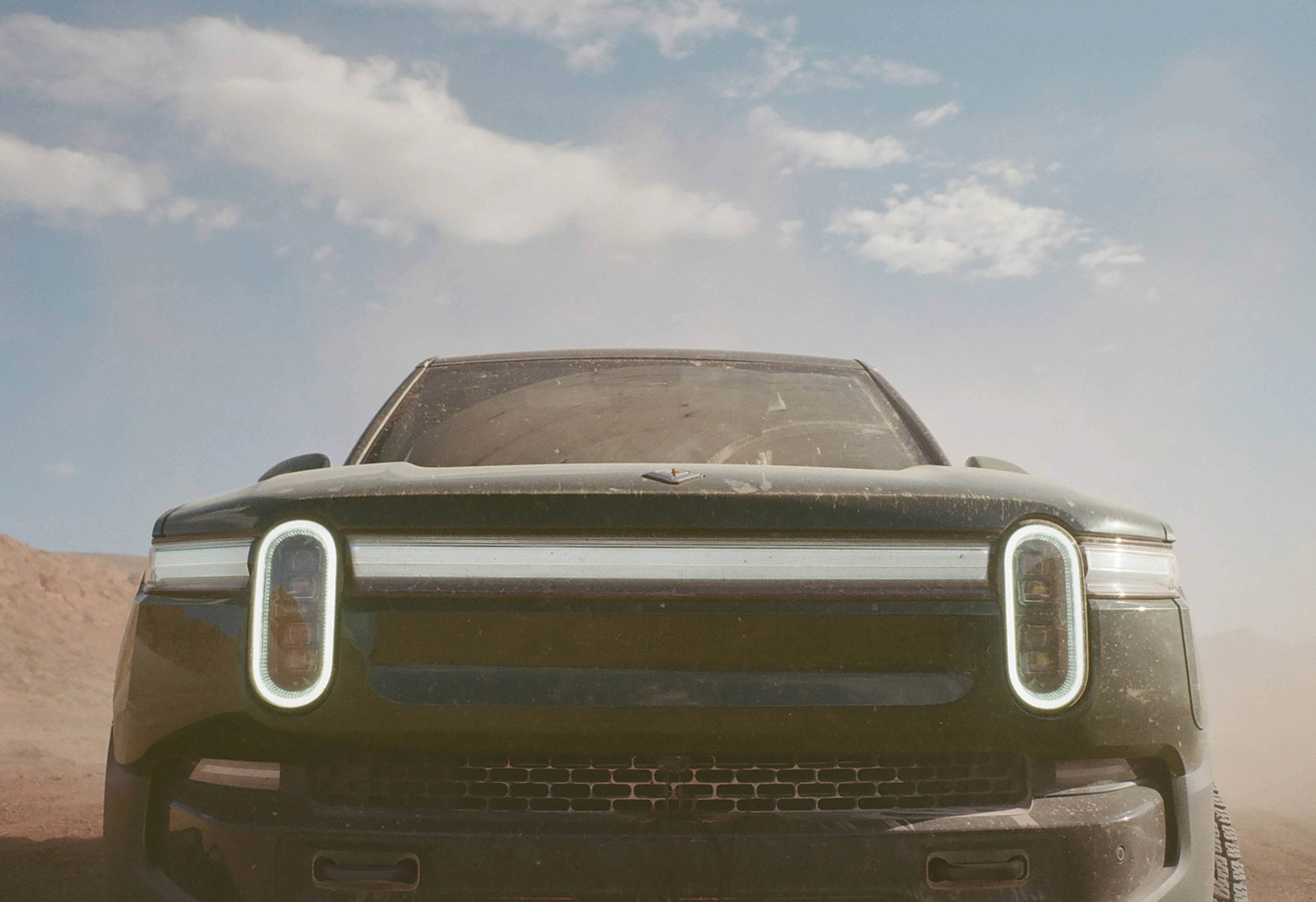 A close up view of the front of a Rivian electric vehicle. The car features the limited-edition Launch Green color way.