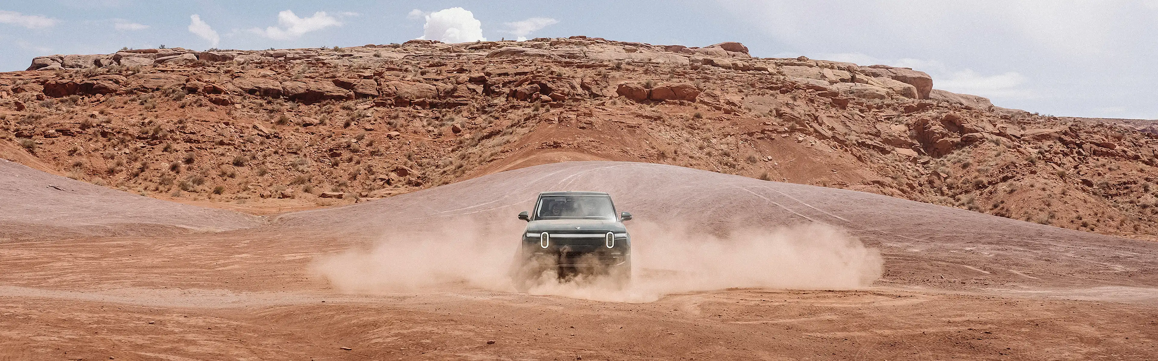 A Rivian electric vehicle performing turns and kicking up dust in a dirt valley.