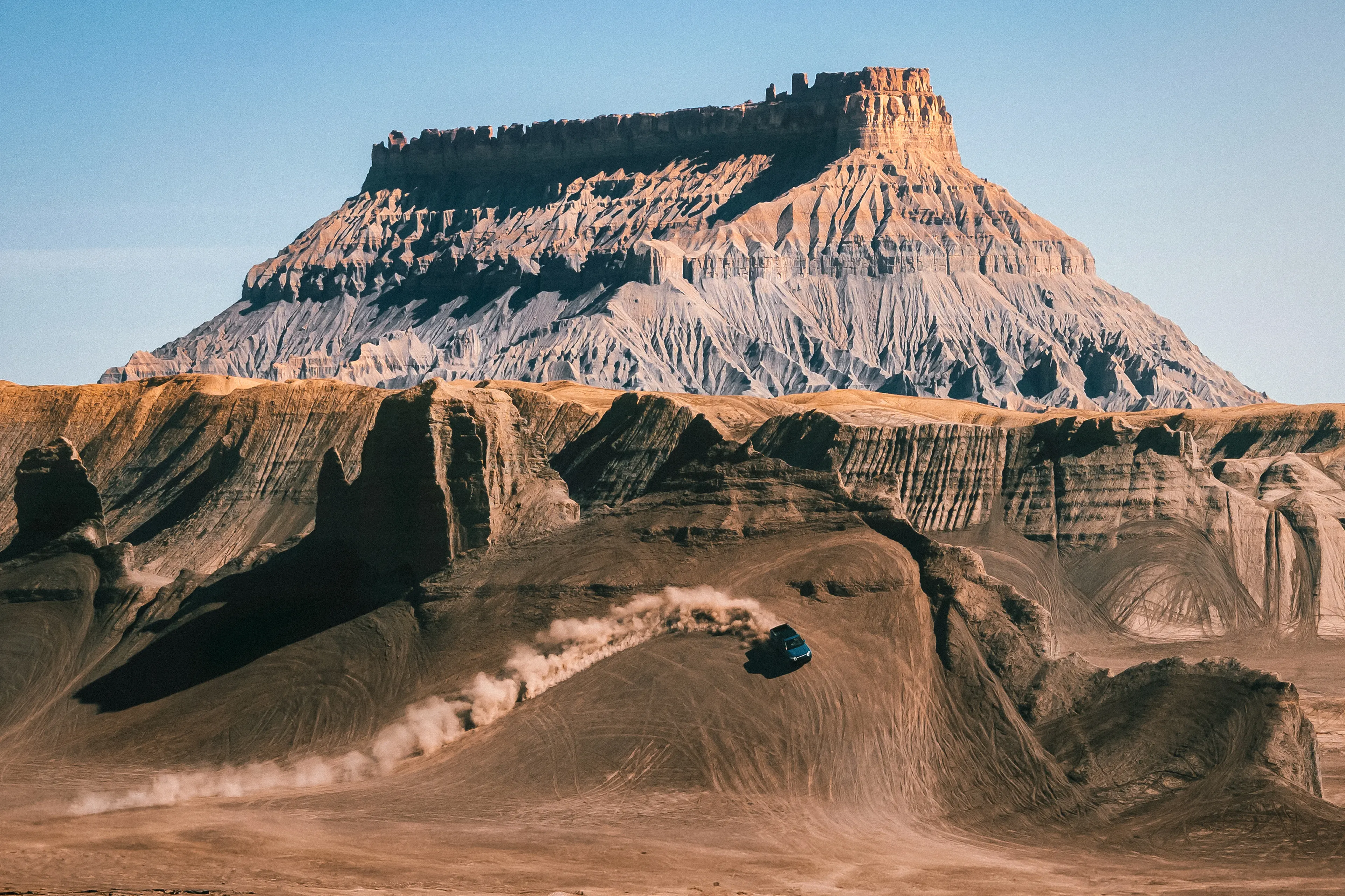 A Rivian electric vehicle performing an impressive turn up the side of a steep cliff. A trail of dust shows the path of the cliff turn.
